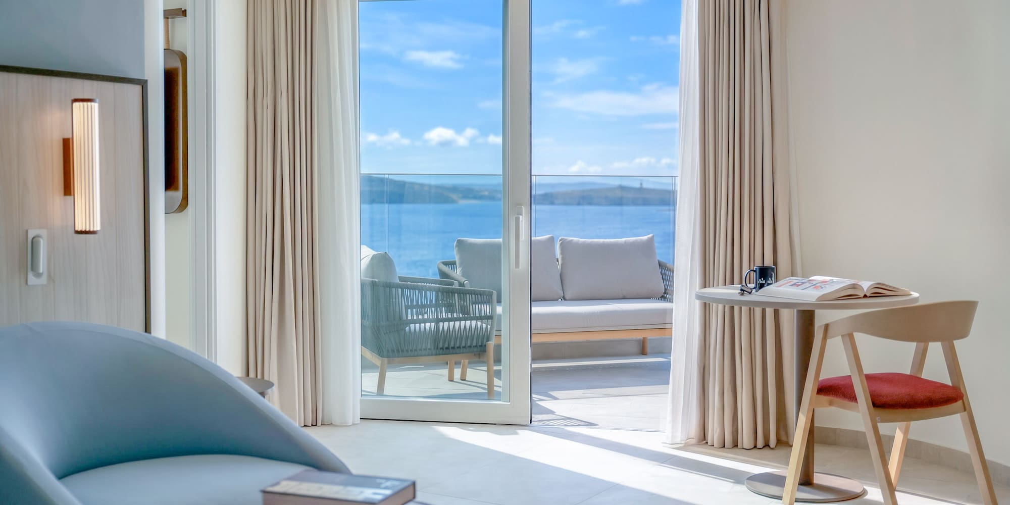 Modern hotel suite with sea view balcony and outdoor lounge furniture.