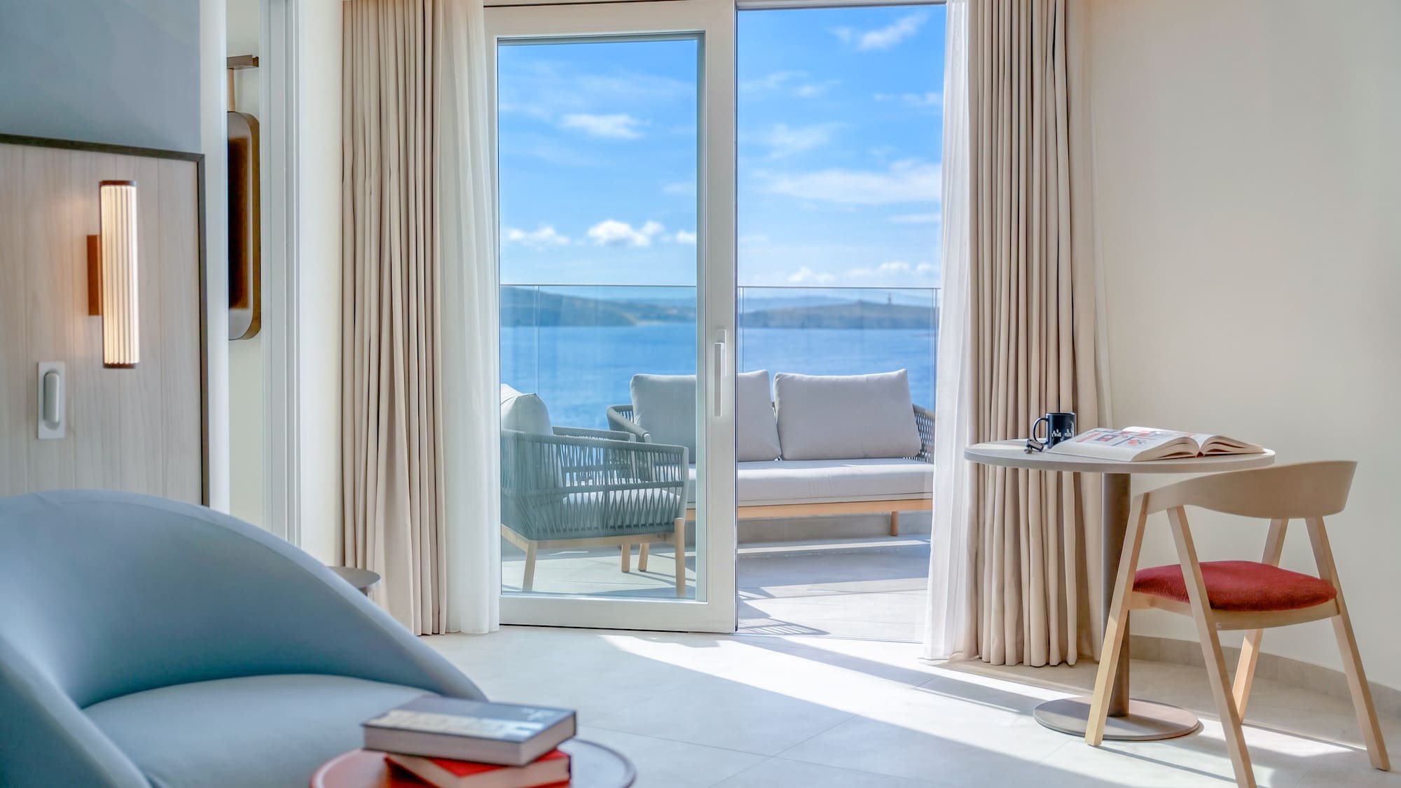 Modern hotel suite with sea view balcony and outdoor lounge furniture.