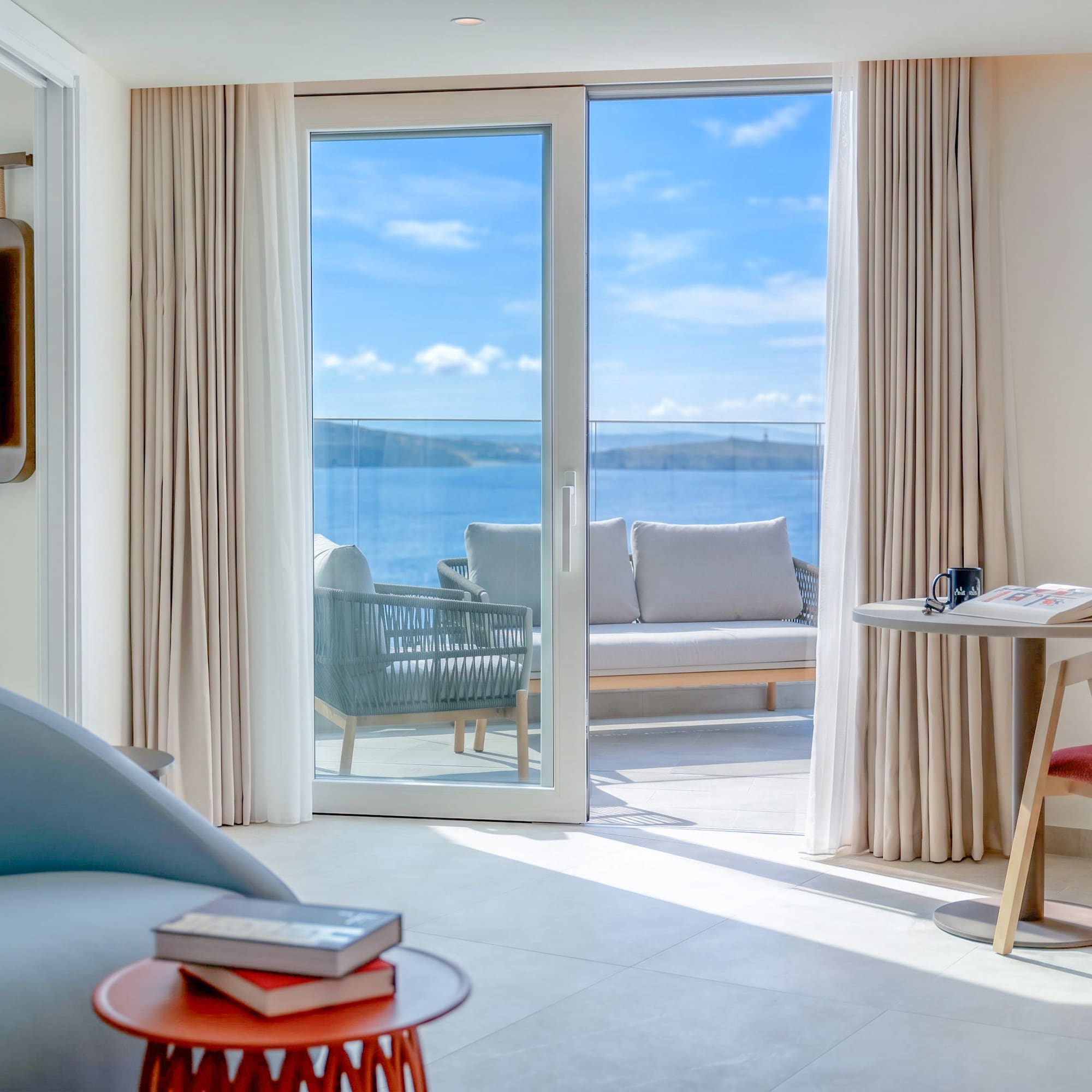 Modern hotel suite with sea view balcony and outdoor lounge furniture.