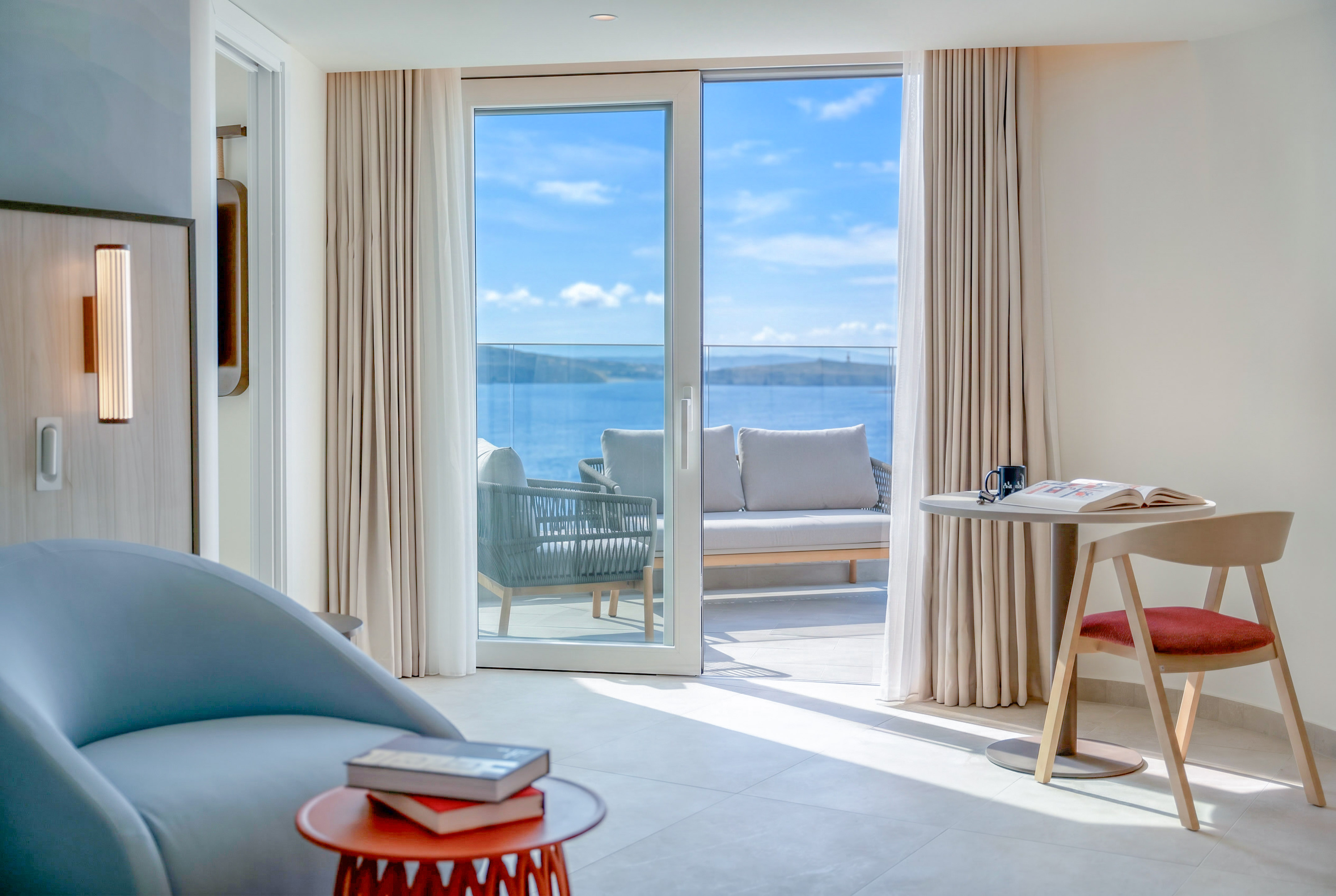 Modern hotel suite with sea view balcony and outdoor lounge furniture.