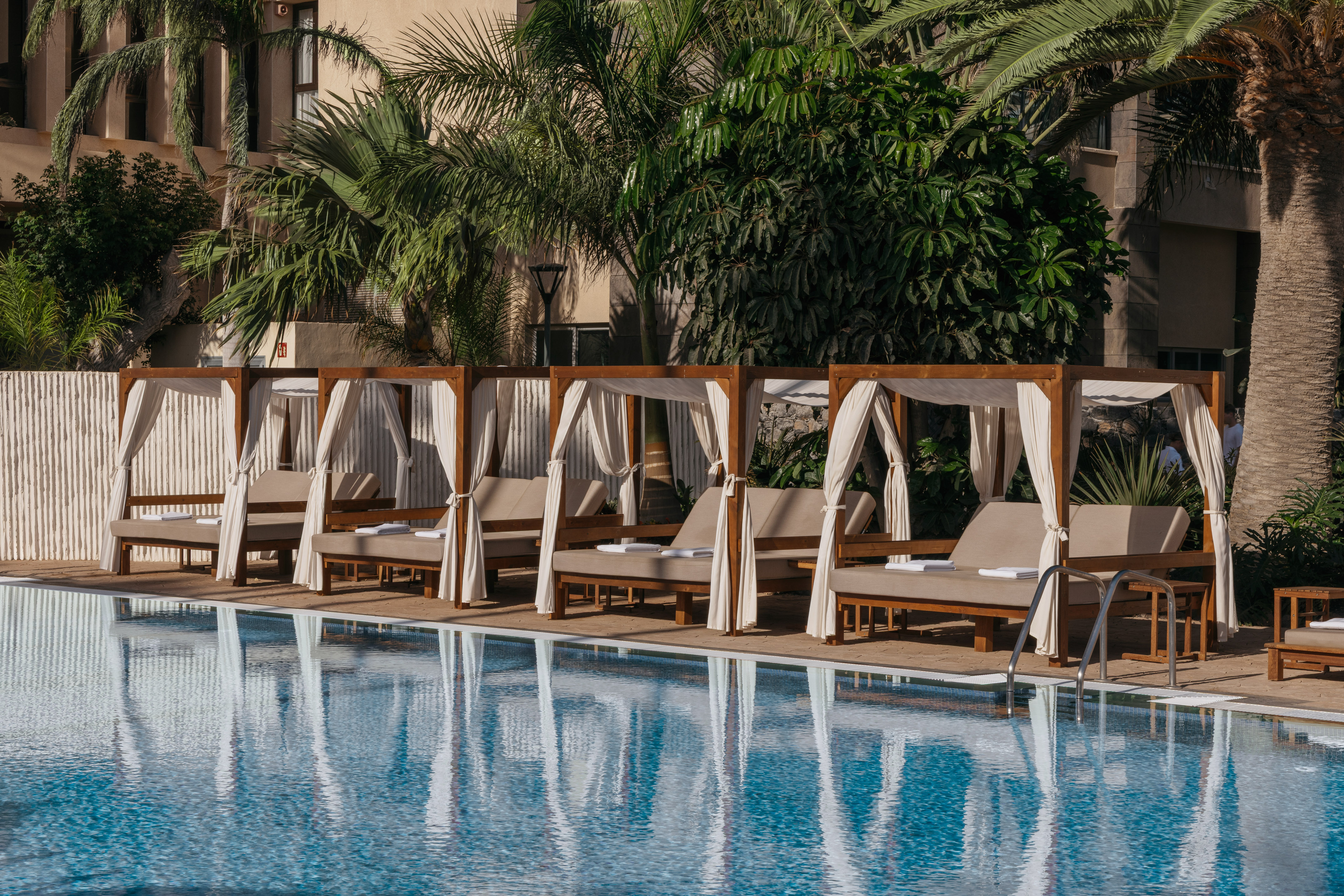 Poolside canopy daybeds and palm trees at a tropical resort.