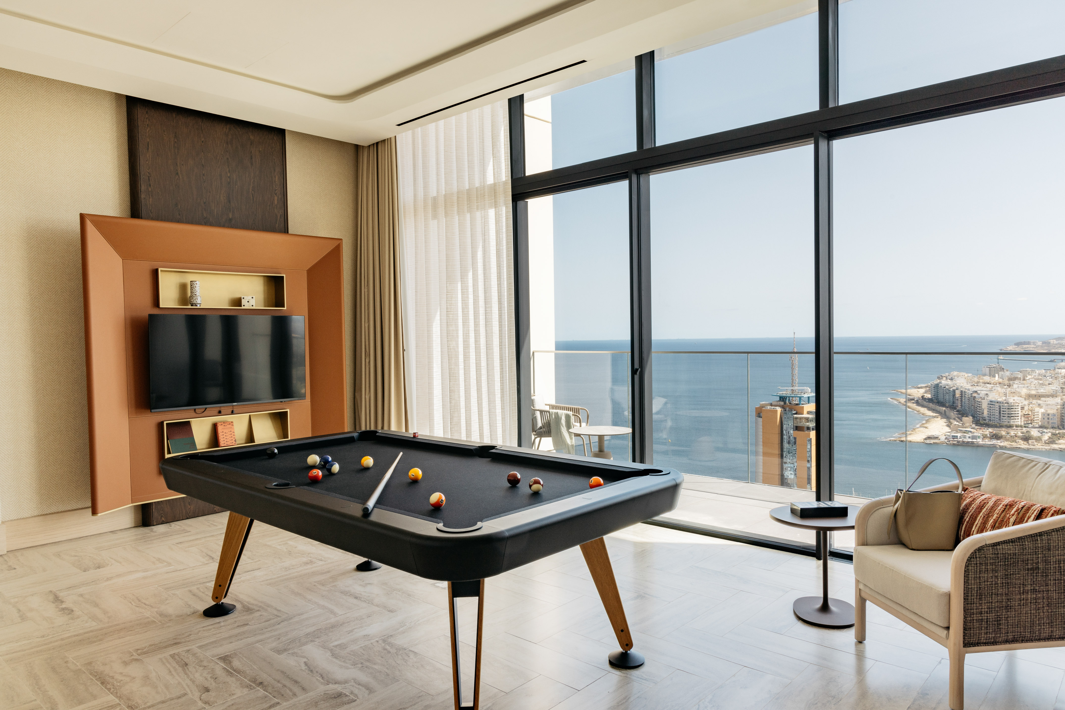 Luxury suite with pool table and panoramic ocean views from large windows.