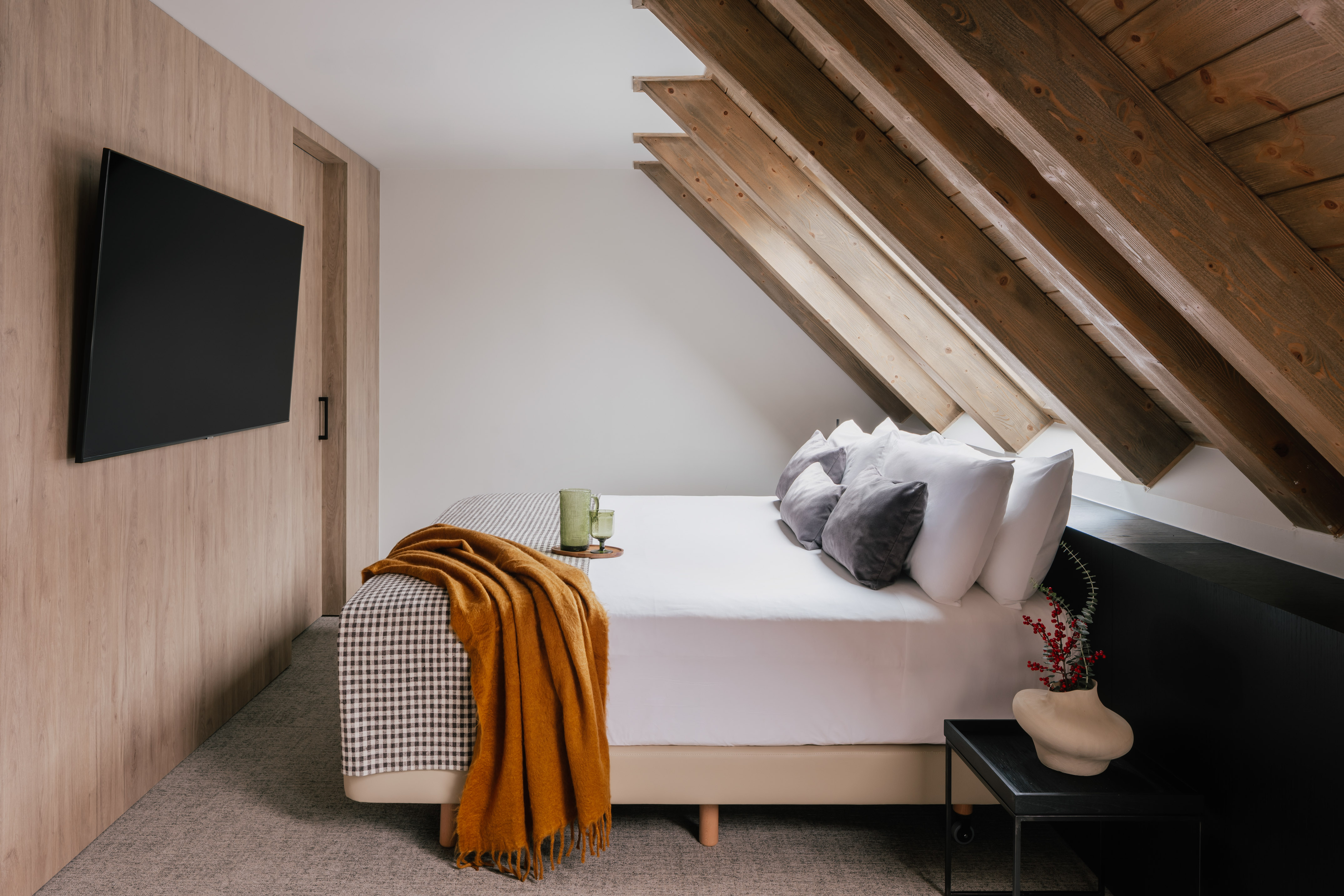 Modern bedroom with slanted wooden ceiling, white bed, orange throw, and TV.