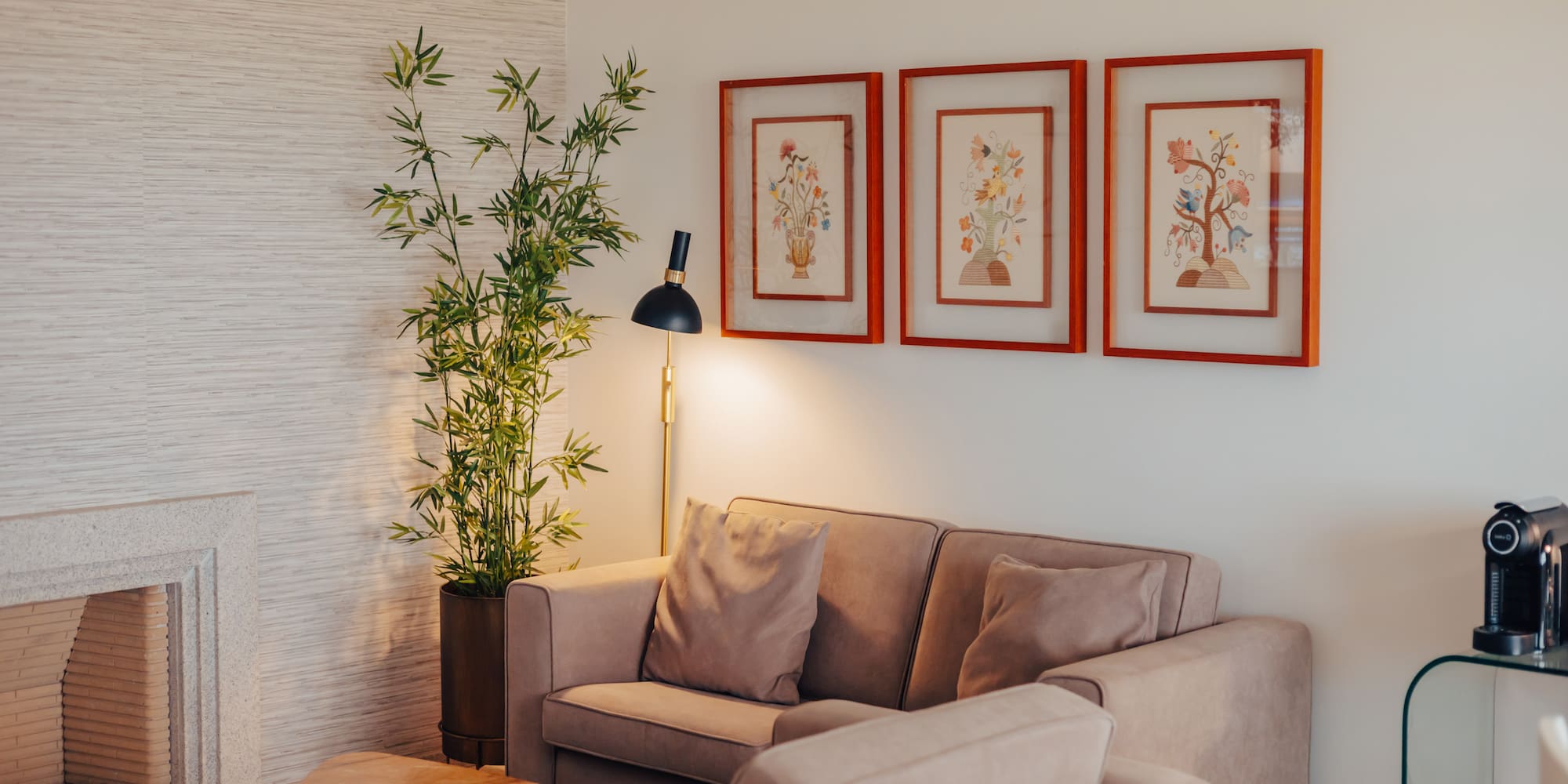 Modern living room with beige sofa, stone fireplace, bamboo plant, and floral art.