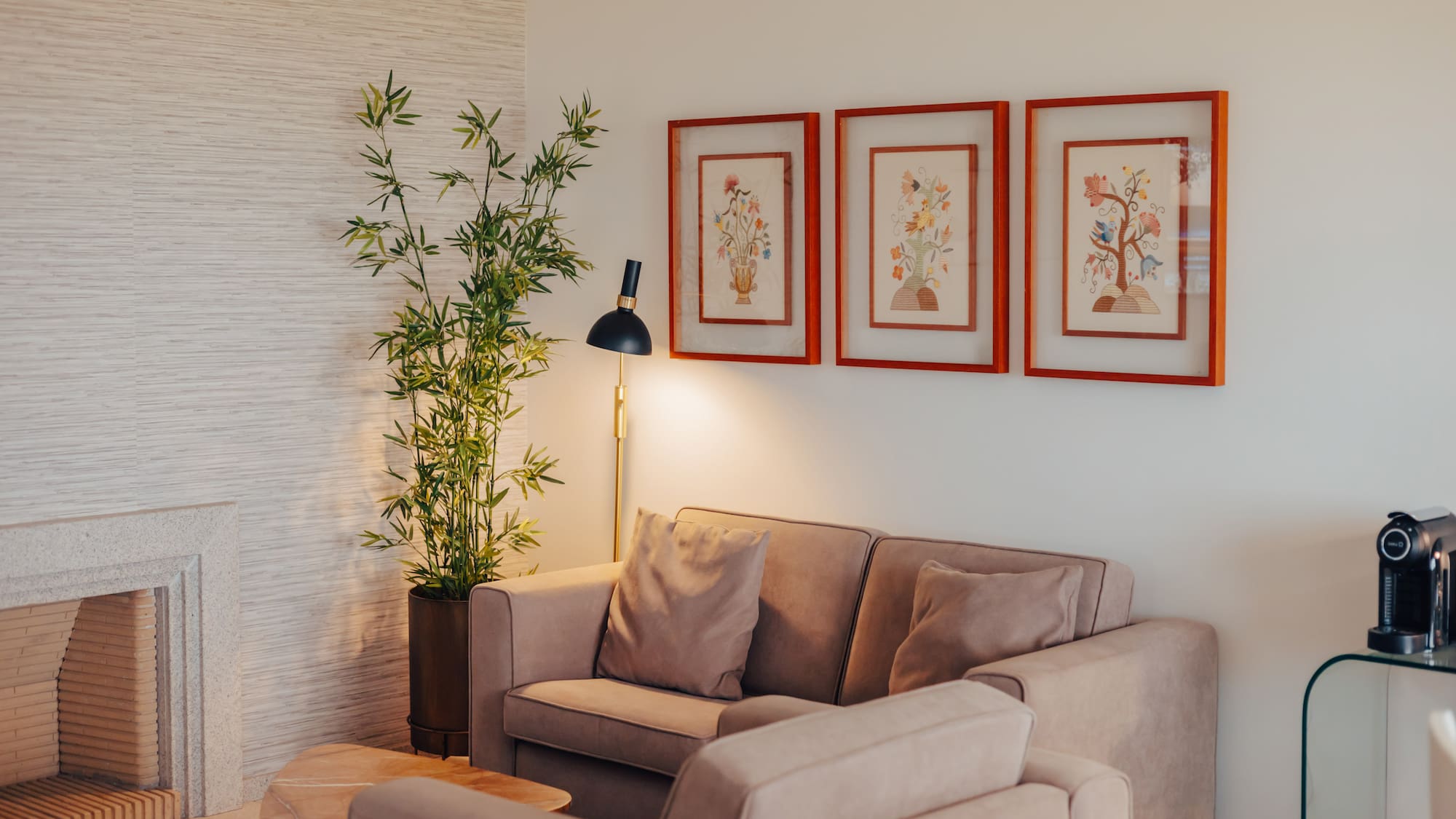 Modern living room with beige sofa, stone fireplace, bamboo plant, and floral art.