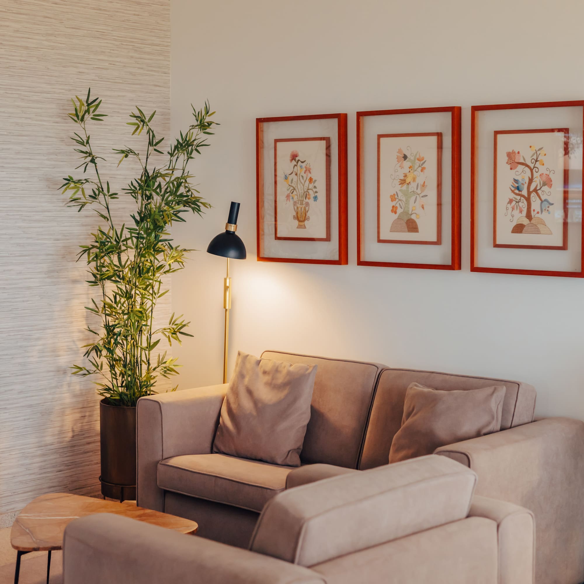 Modern living room with beige sofa, stone fireplace, bamboo plant, and floral art.