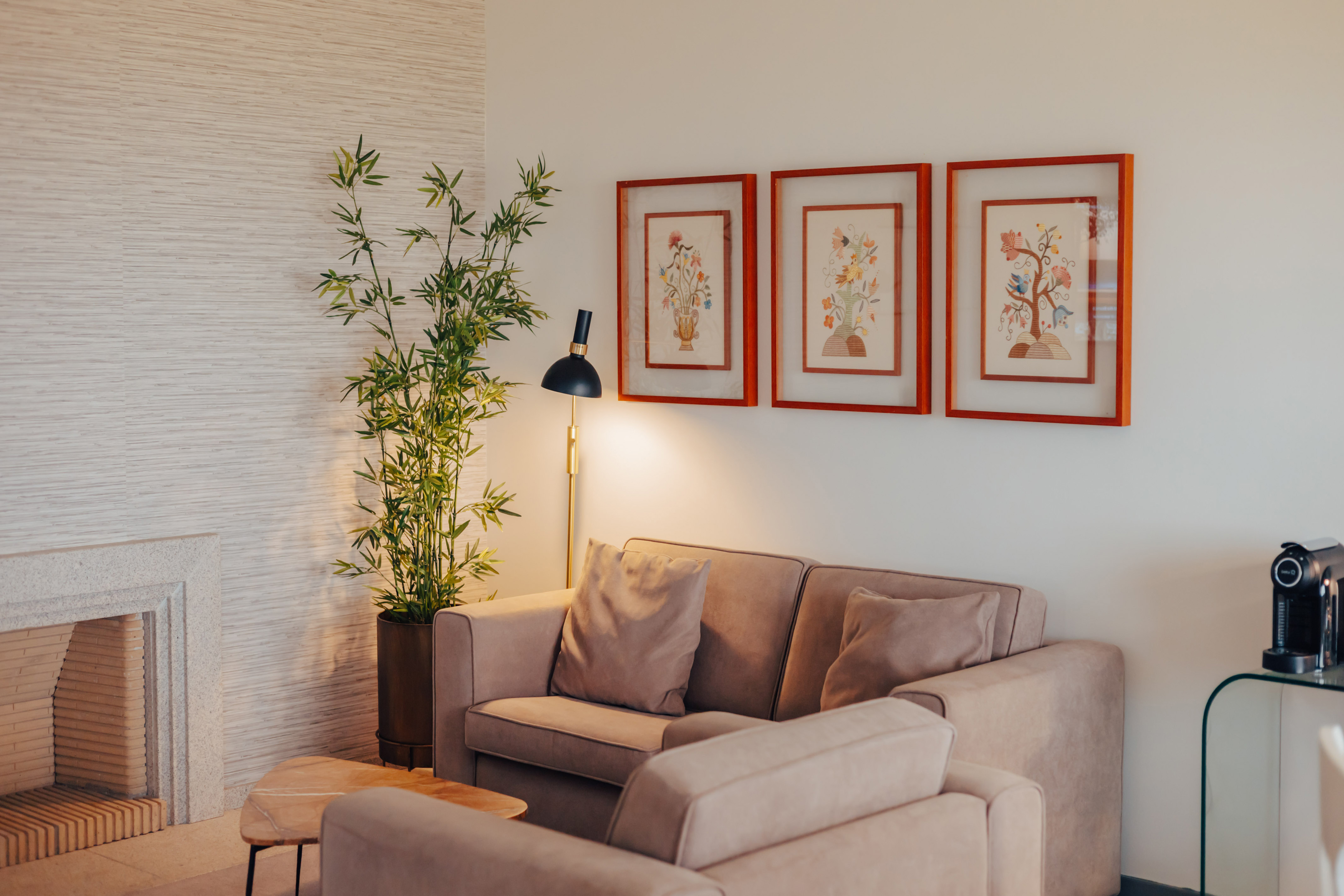 Modern living room with beige sofa, stone fireplace, bamboo plant, and floral art.