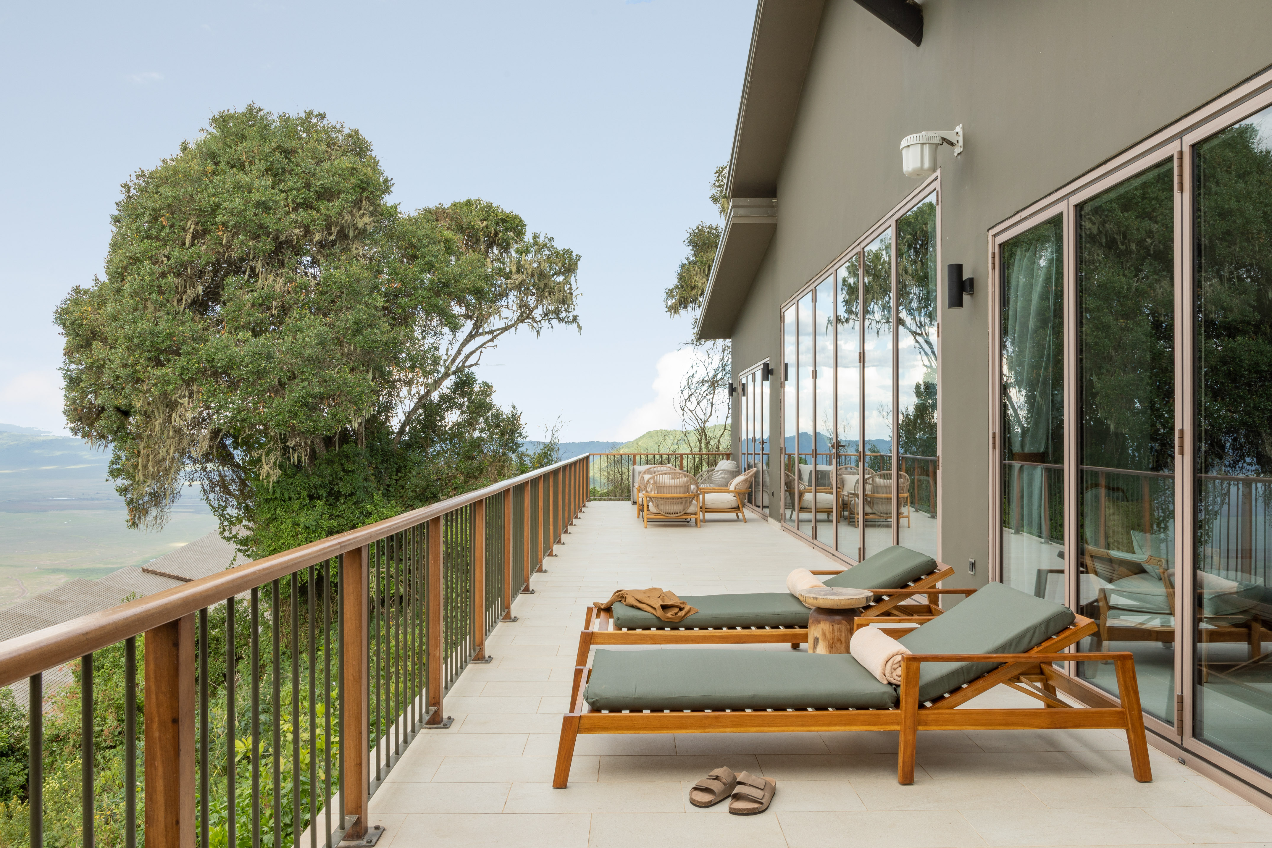 Lodge balcony with lounge chairs, stunning view of crater and lush trees.
