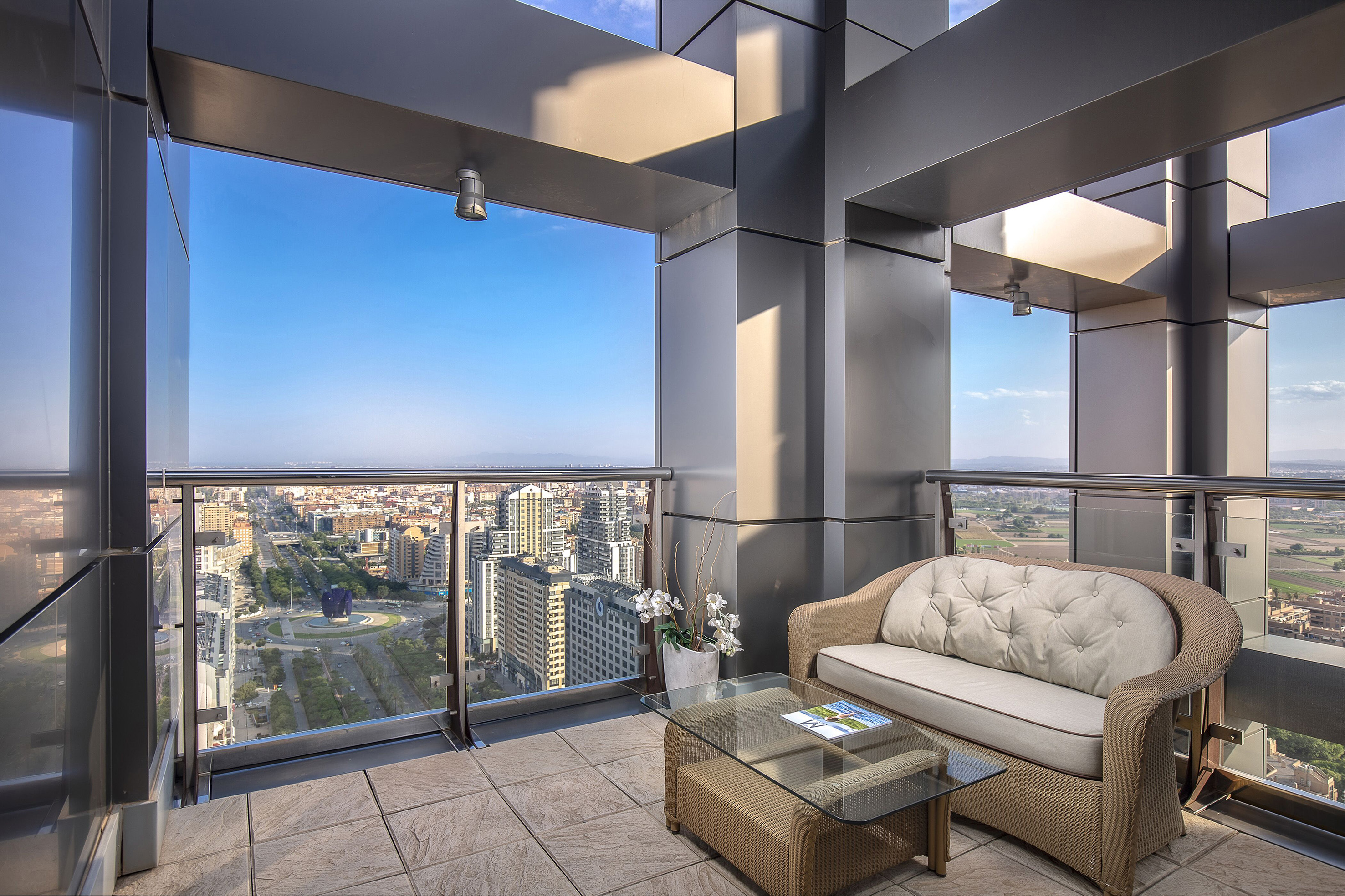 High-rise apartment balcony with city skyline view and wicker sofa.