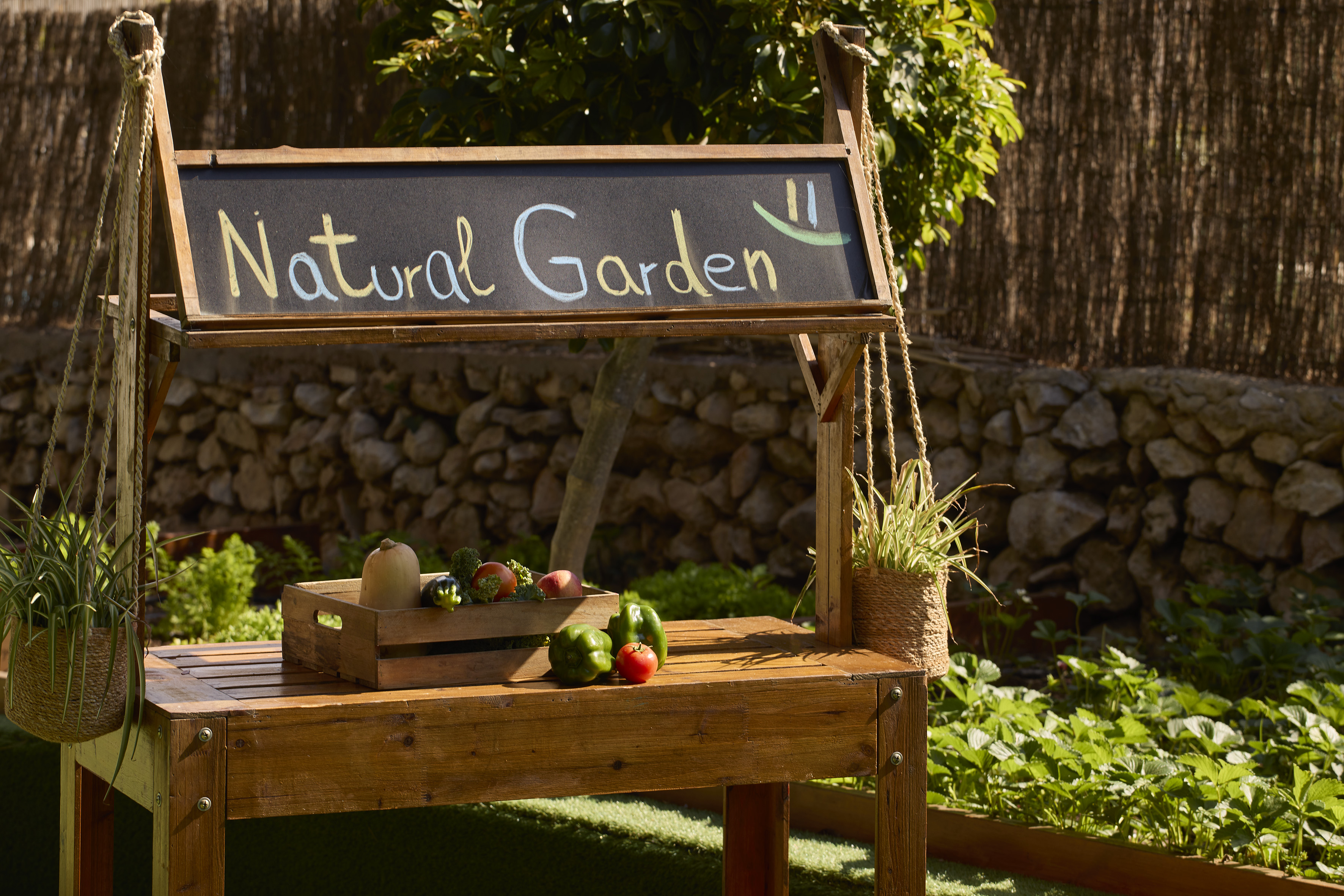 Outdoor "Natural Garden" sign on wooden stand with fresh vegetables.