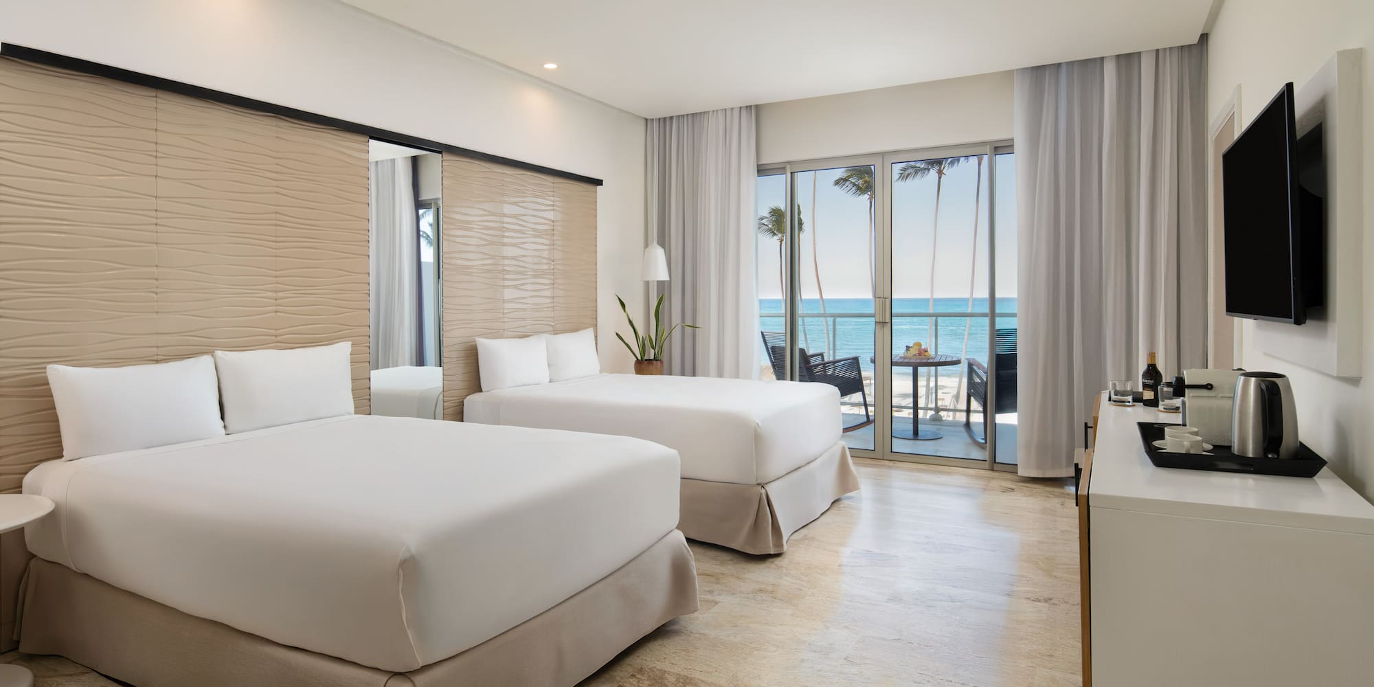 Modern hotel room with two beds, oceanfront view, and private balcony.