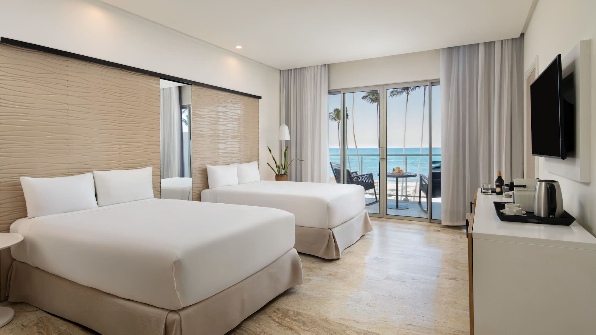 Modern hotel room with two beds, oceanfront view, and private balcony.