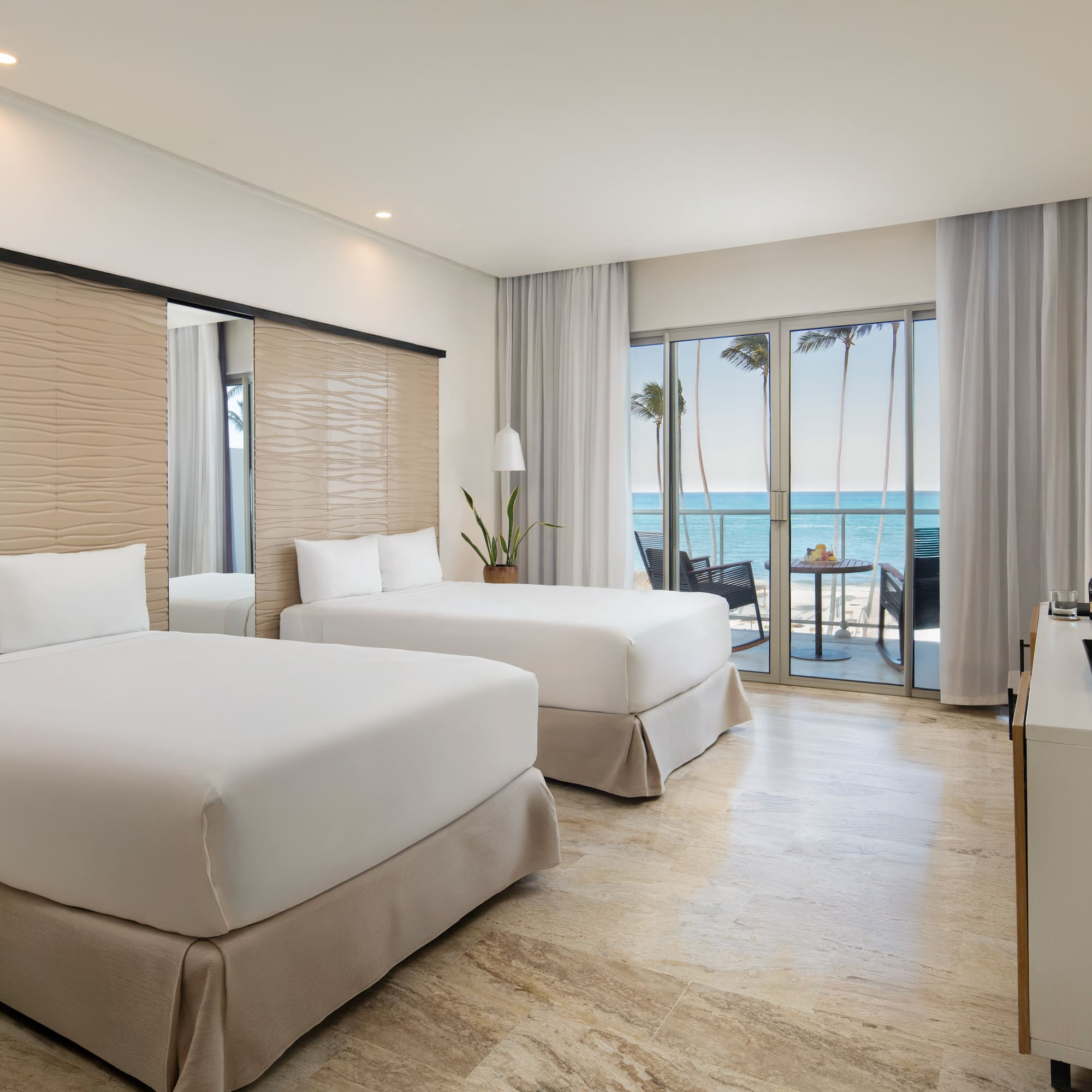 Modern hotel room with two beds, oceanfront view, and private balcony.