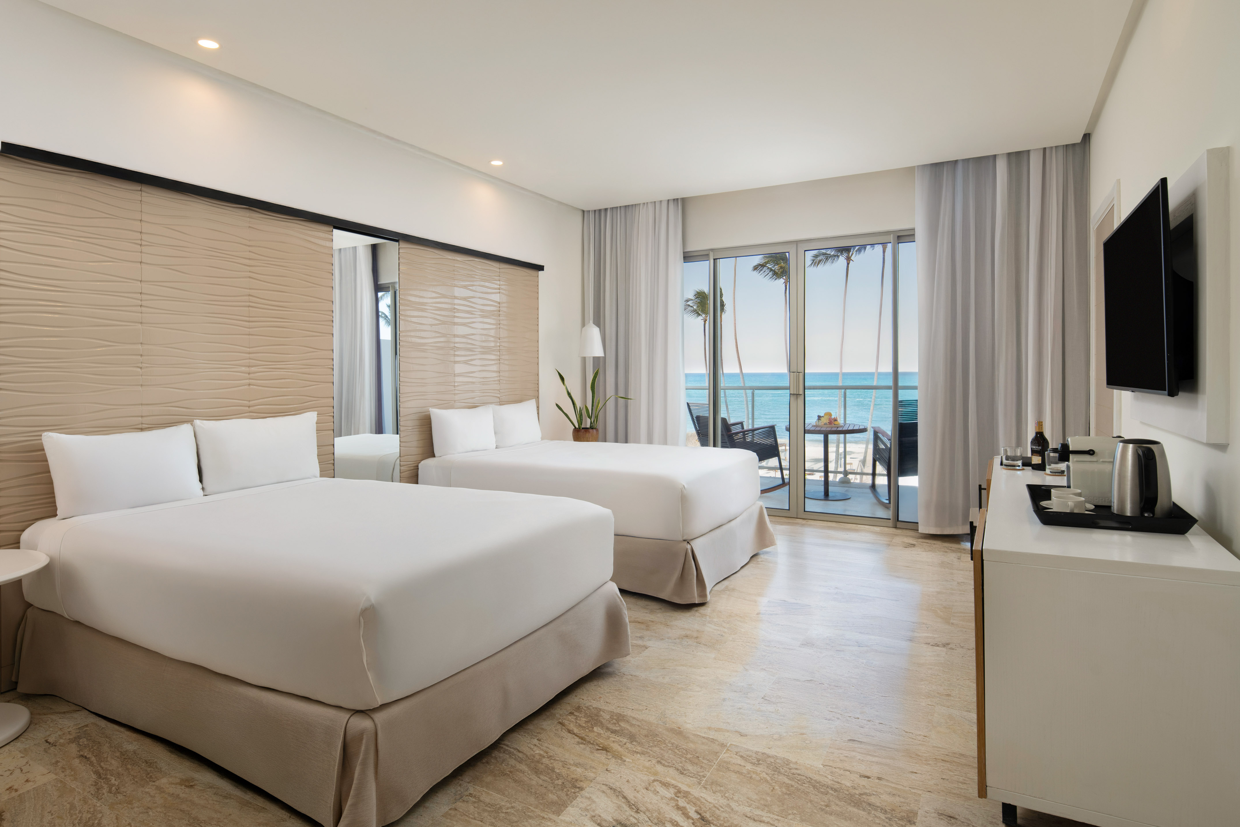Modern hotel room with two beds, oceanfront view, and private balcony.