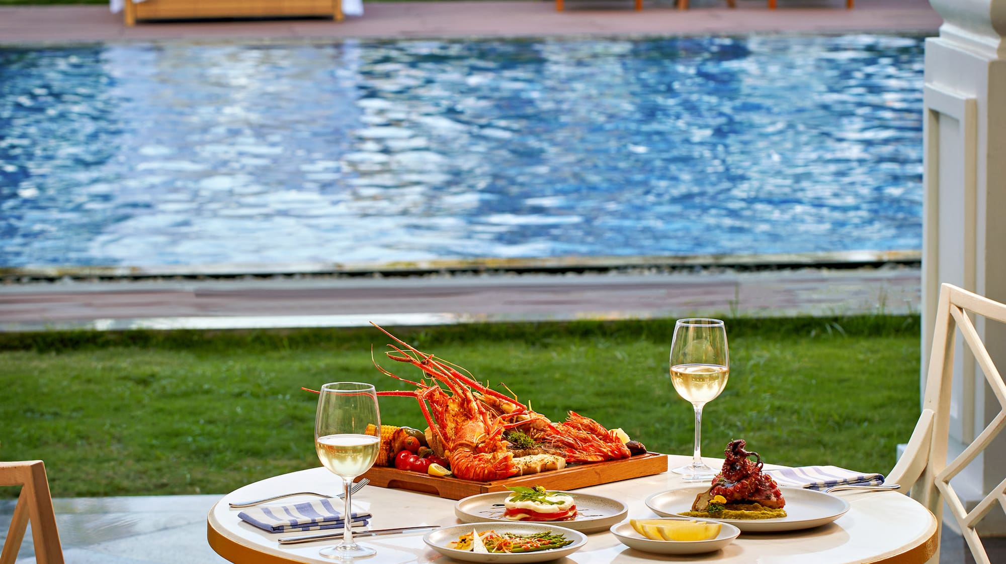 a table with food and wine glasses on it by a pool