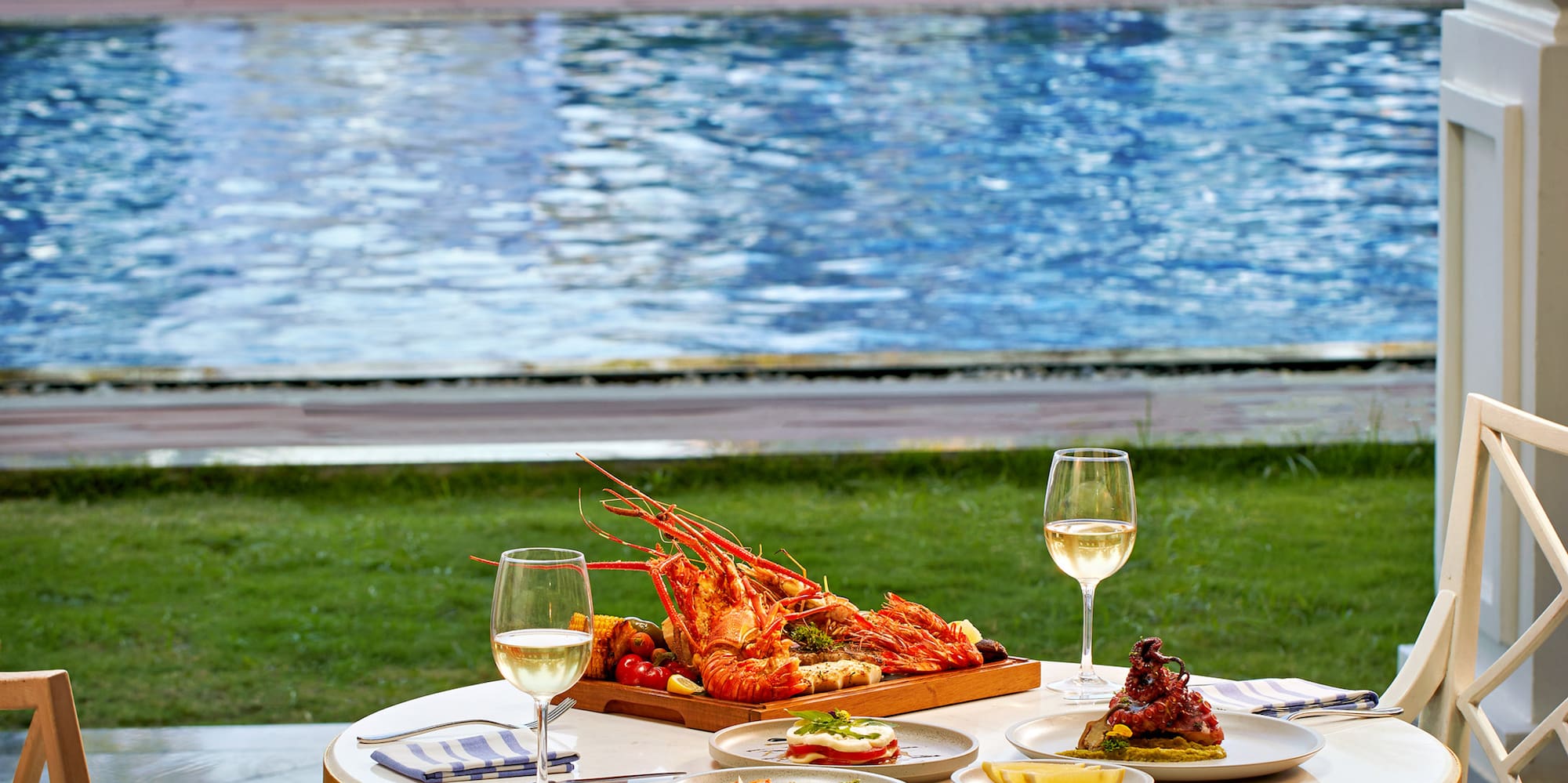 a table with food and wine glasses on it by a pool
