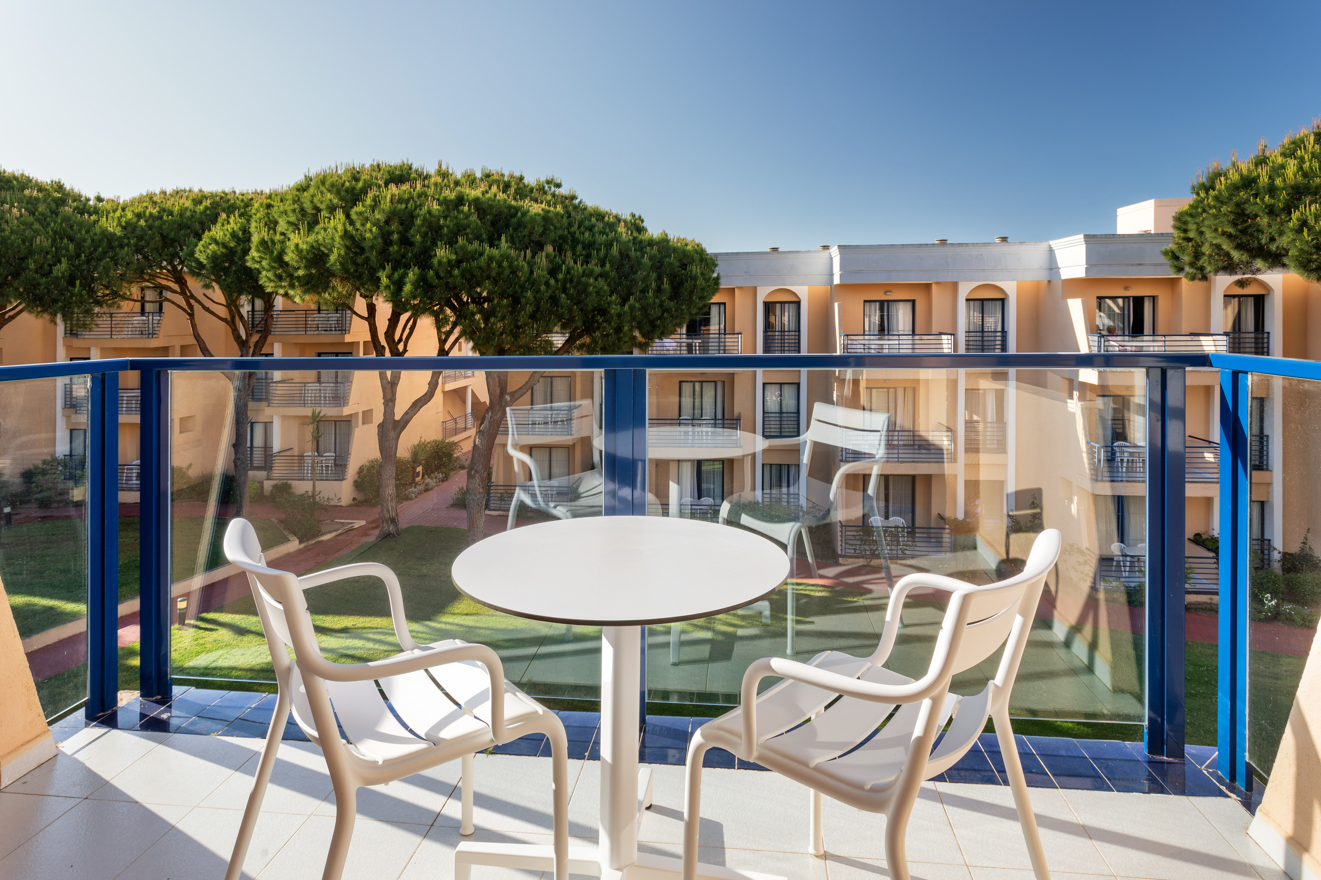 Hotel balcony with outdoor seating, resort buildings, and pine trees.