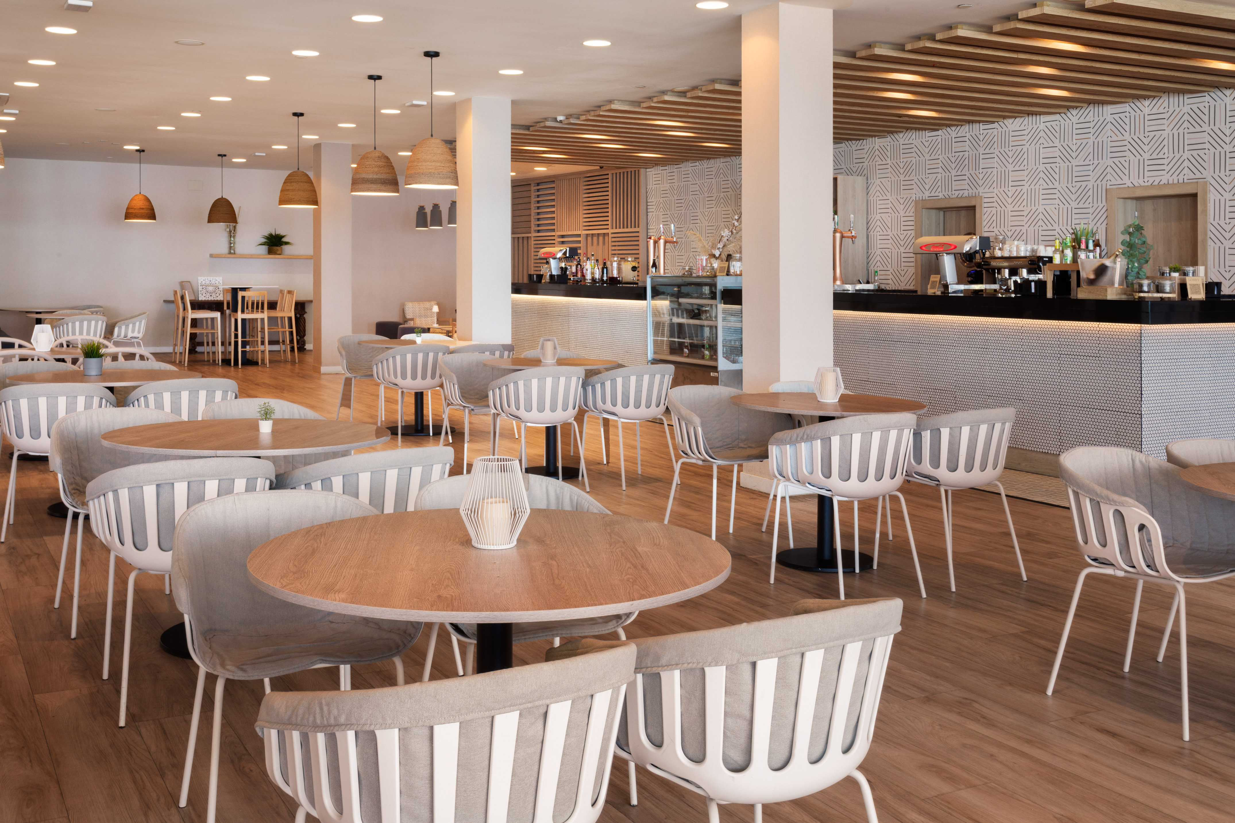 Modern cafe interior with stylish round tables, grey chairs, and a coffee bar.