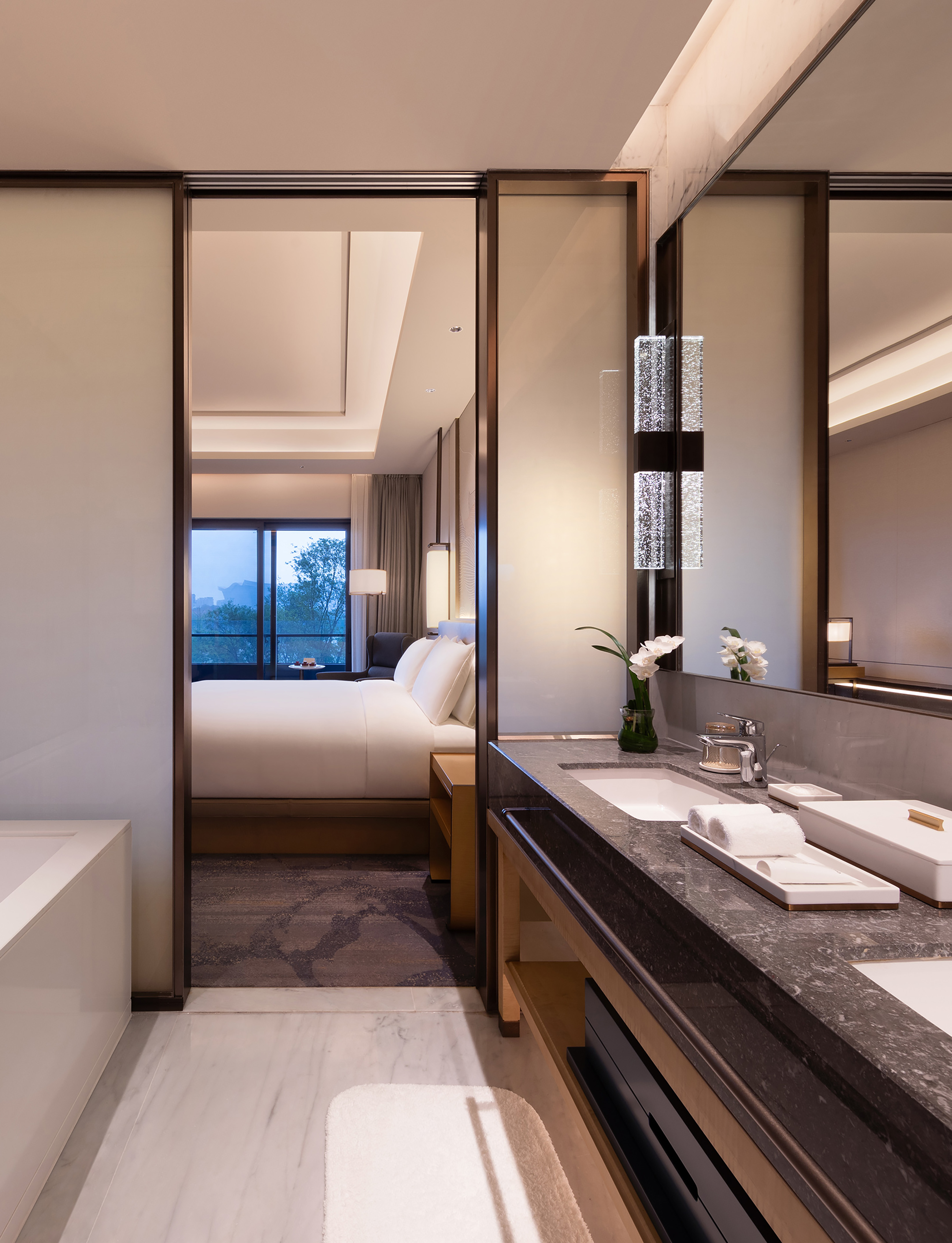 Hotel suite bathroom with double vanity next to a modern bedroom.