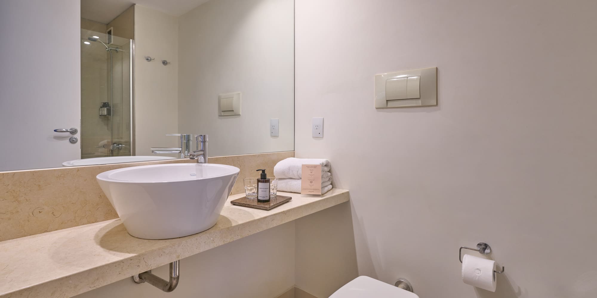 Modern bathroom with white vessel sink, marble vanity, toilet, and shower reflection.