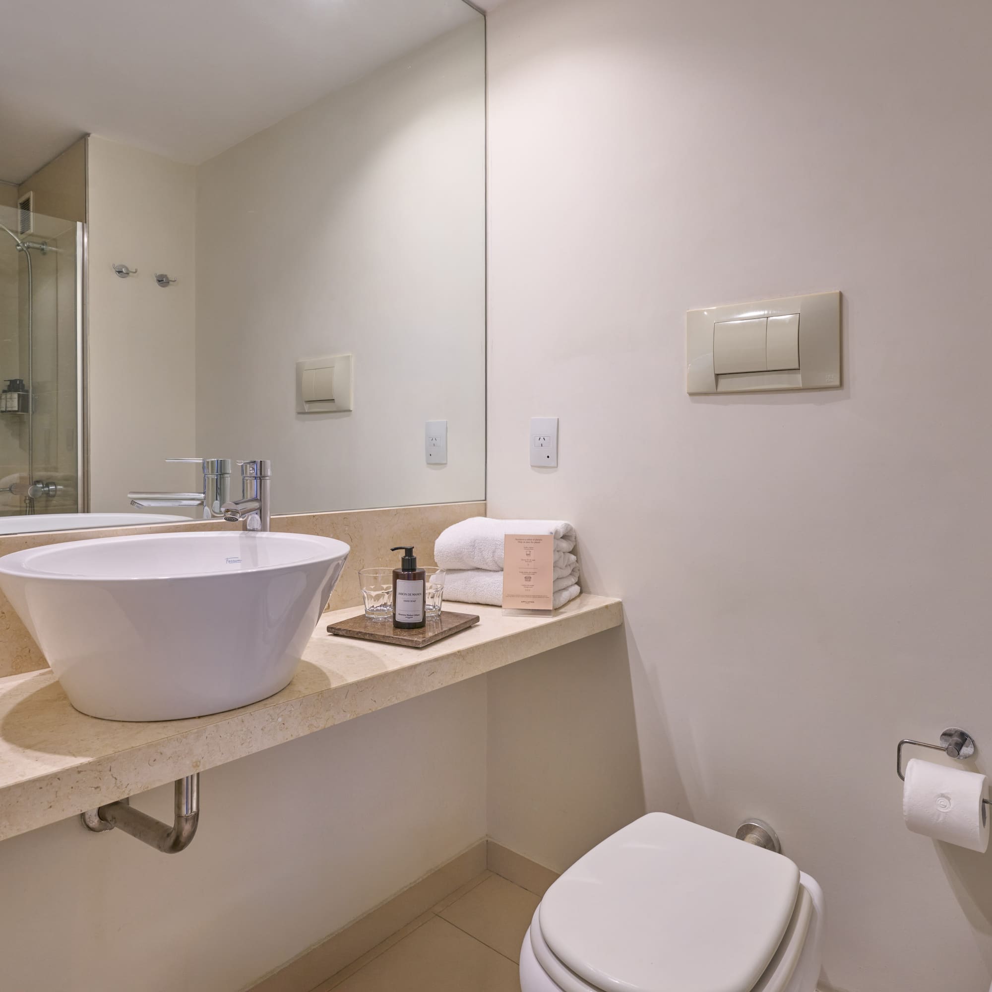 Modern bathroom with white vessel sink, marble vanity, toilet, and shower reflection.