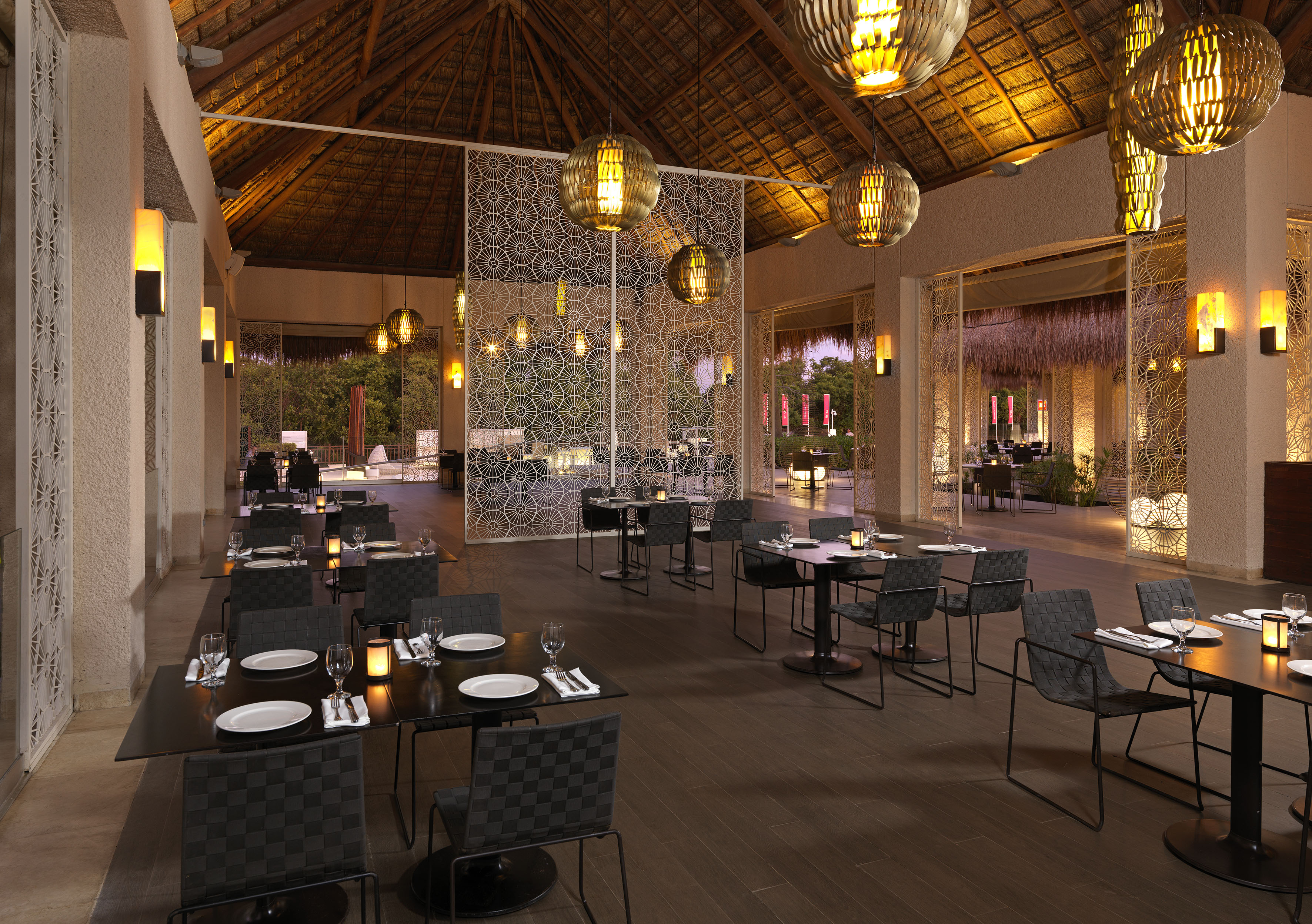 Tropical restaurant with thatched roof, warm lighting, and elegant dining tables.