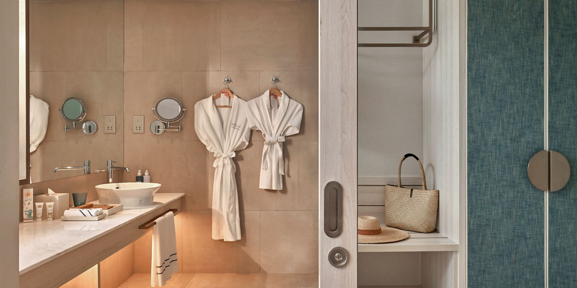 Meliá hotel bathroom with modern vanity, white robes, and open closet area.