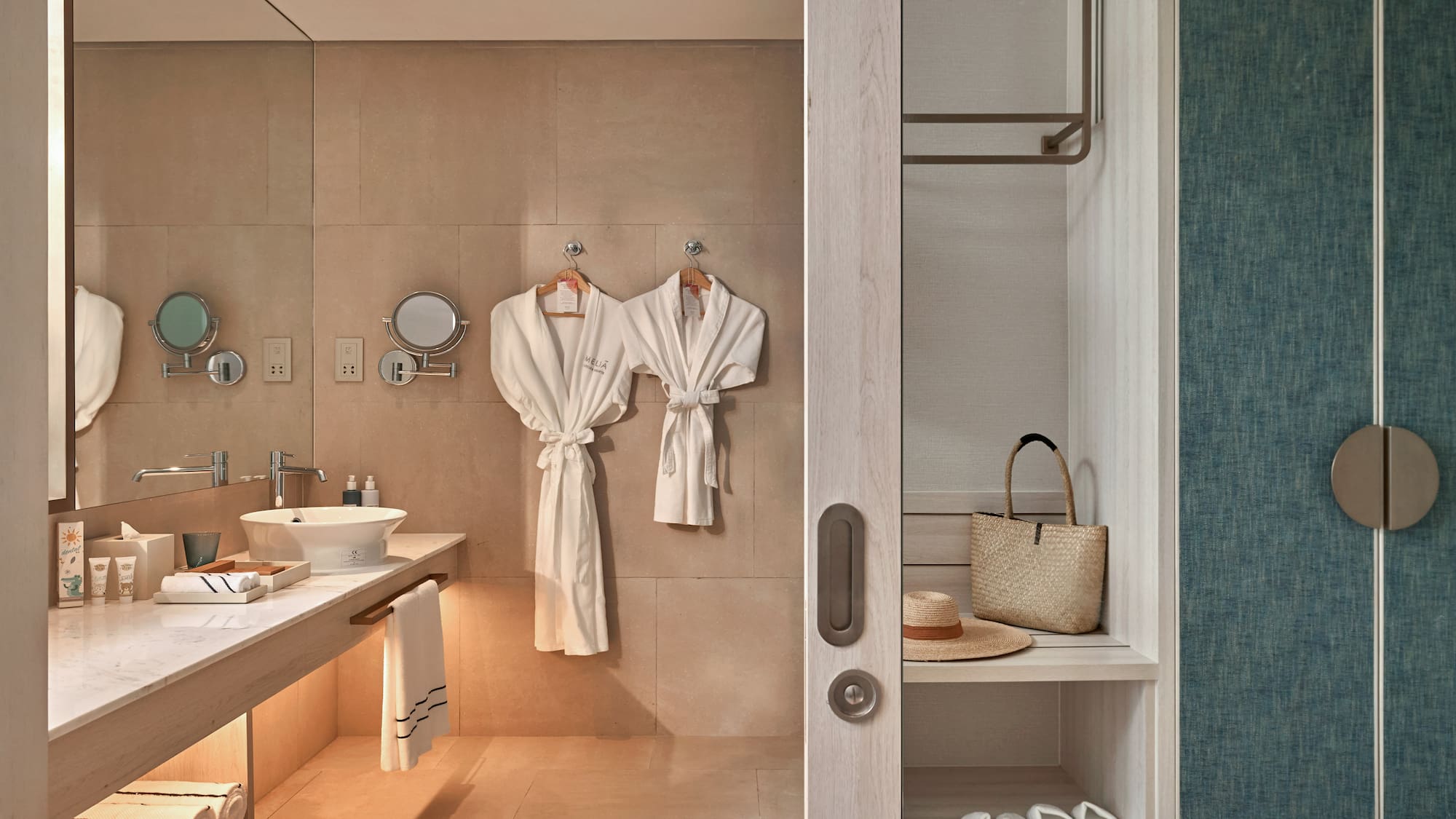 Meliá hotel bathroom with modern vanity, white robes, and open closet area.