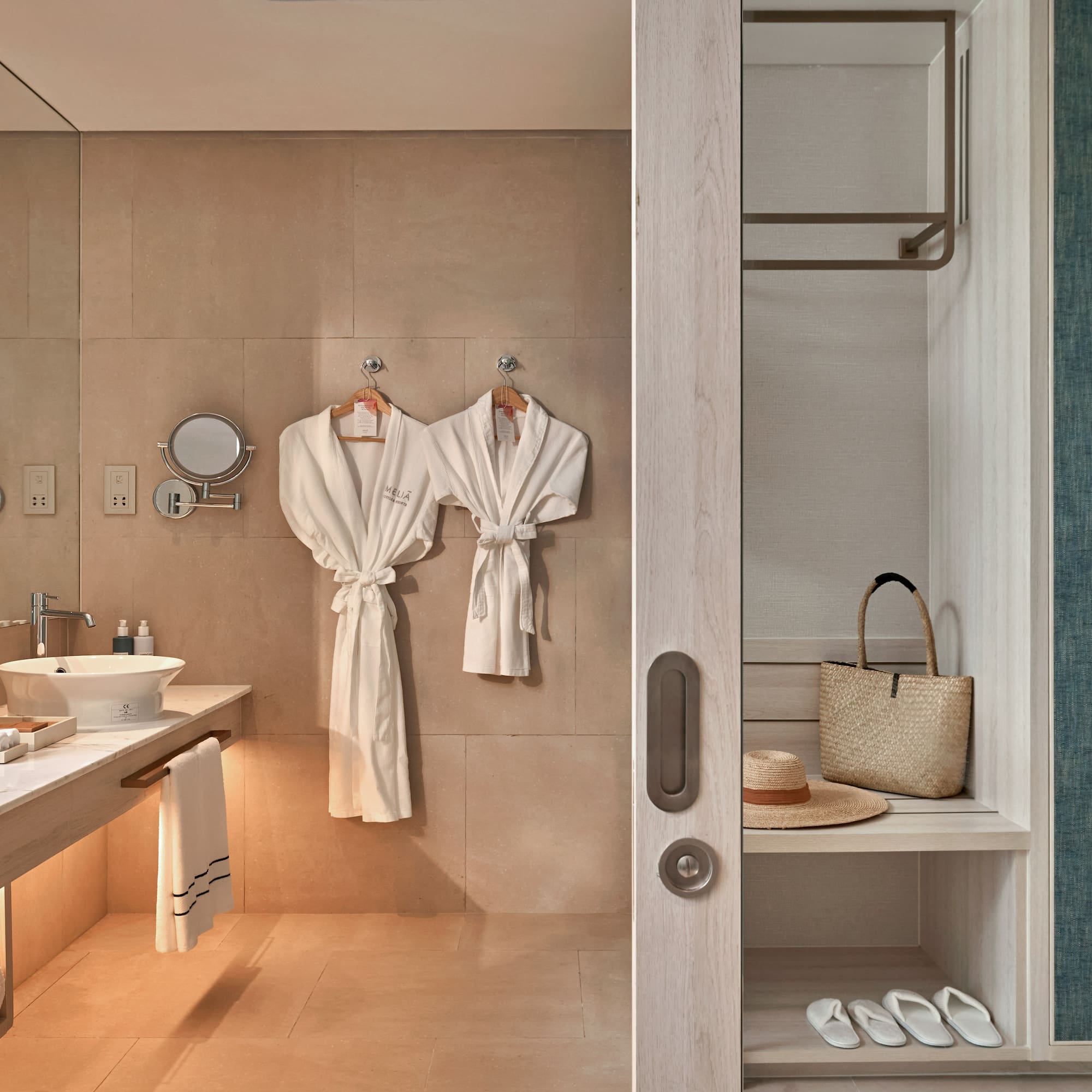 Meliá hotel bathroom with modern vanity, white robes, and open closet area.