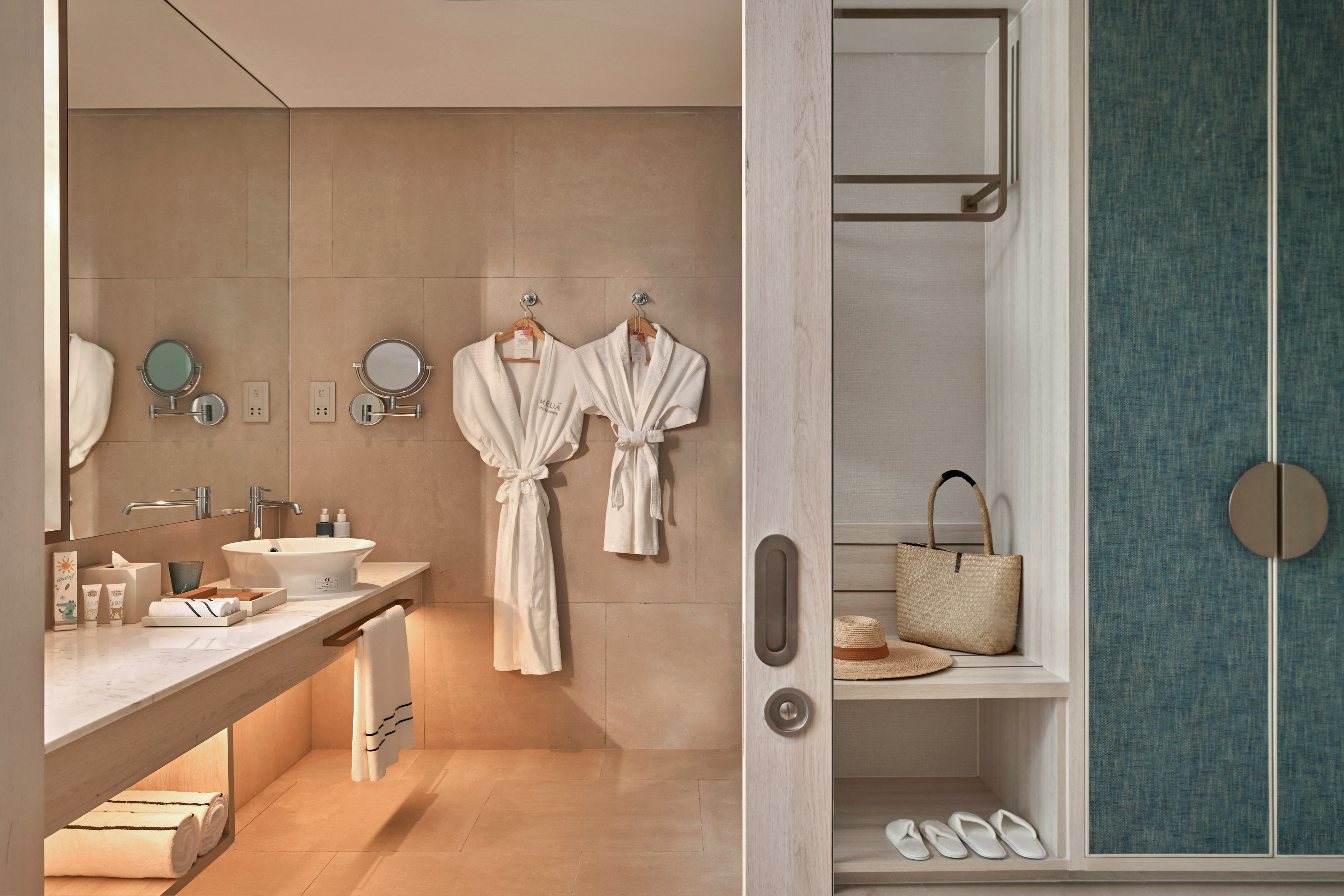 Meliá hotel bathroom with modern vanity, white robes, and open closet area.
