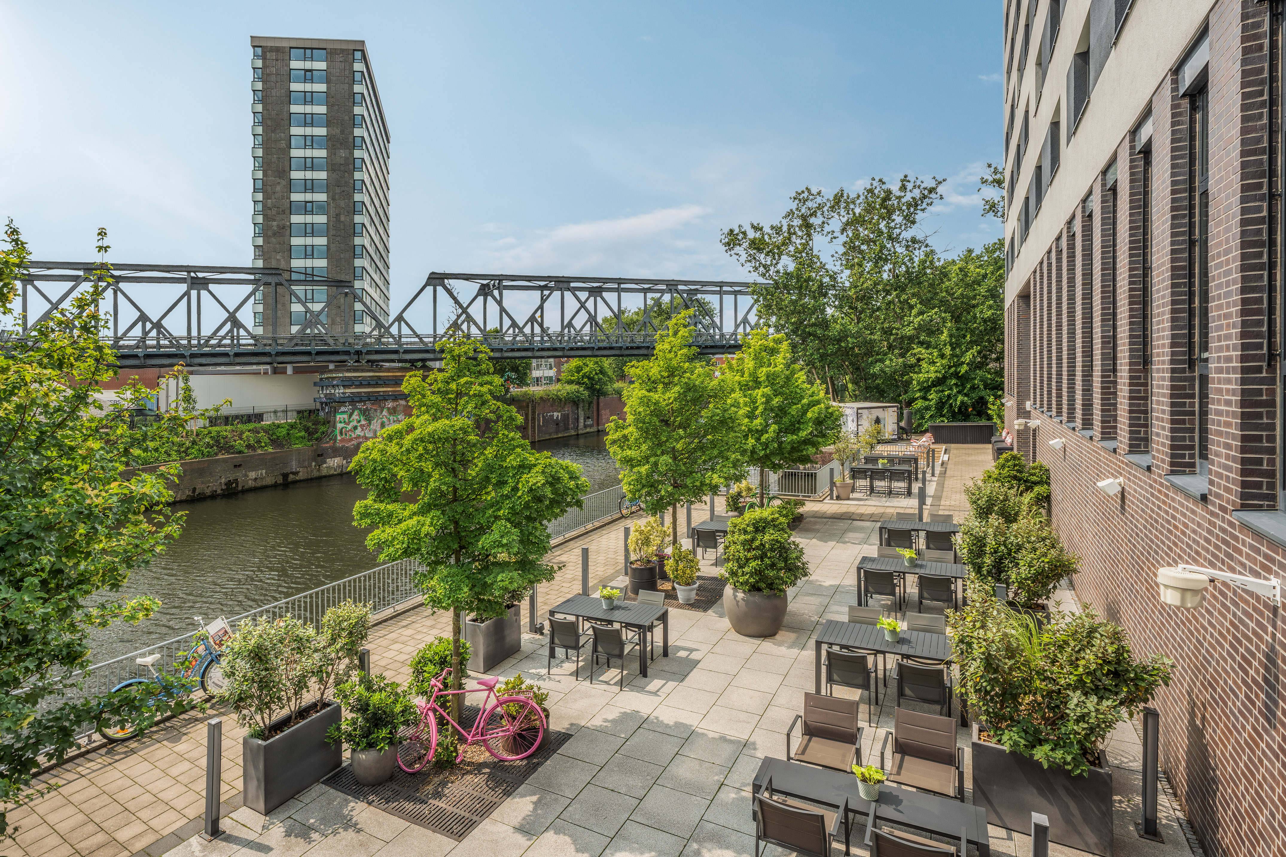 Riverside terrace with al fresco dining tables, urban bridge, and skyscraper. - INNSiDE Hamburg Hafen, Hamburgo