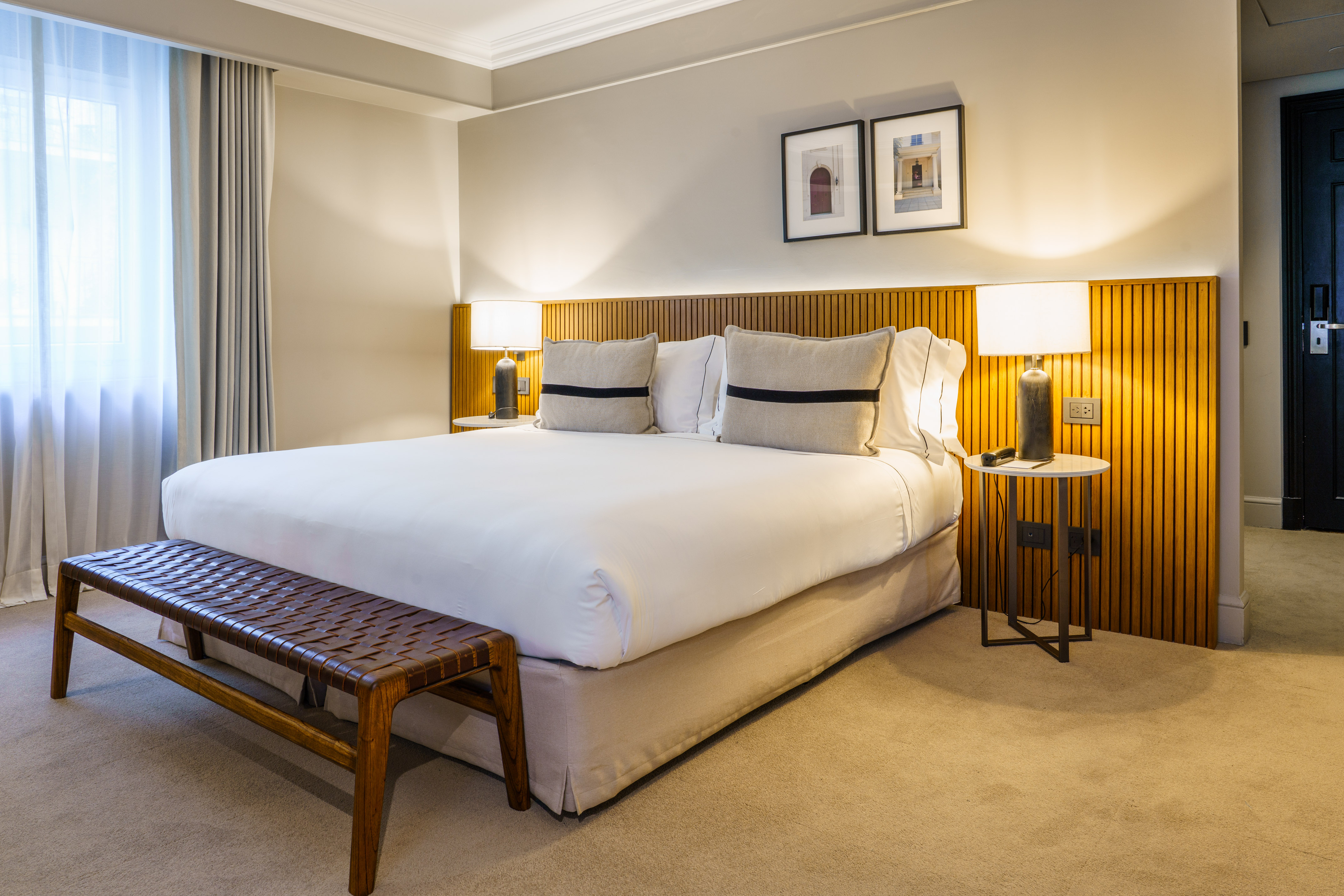 Elegant hotel room with king bed, slatted headboard, and leather bench.