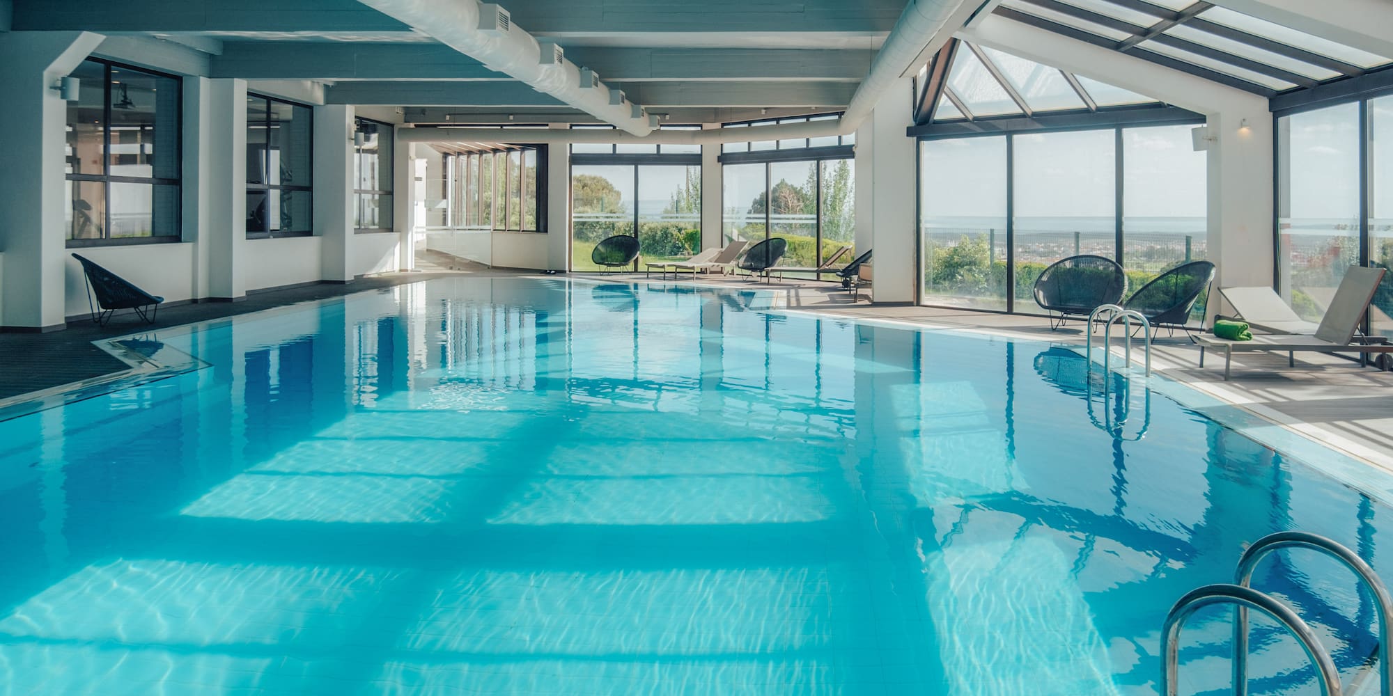 Bright indoor pool with lounge chairs, large windows, and scenic view.