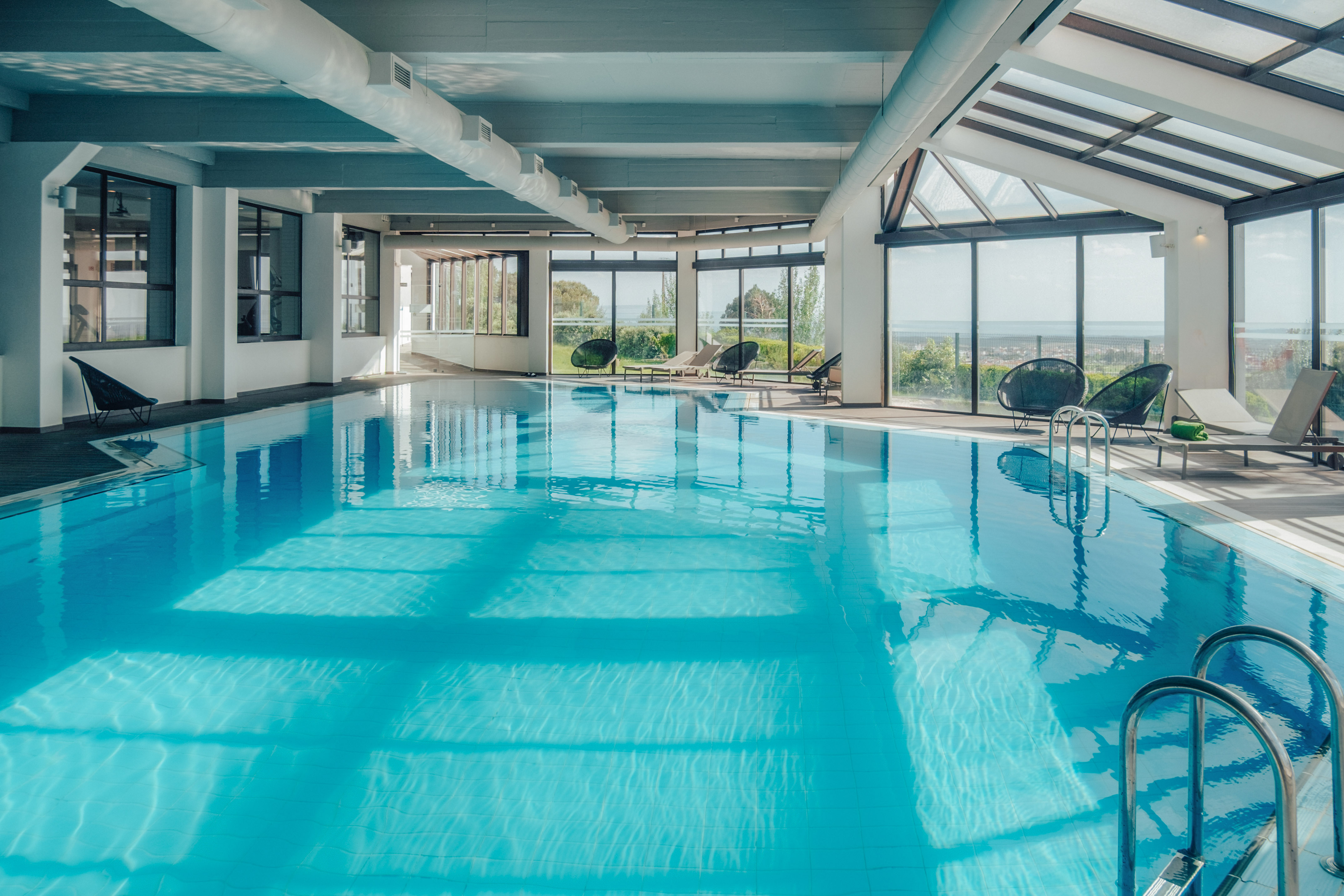 Bright indoor pool with lounge chairs, large windows, and scenic view.
