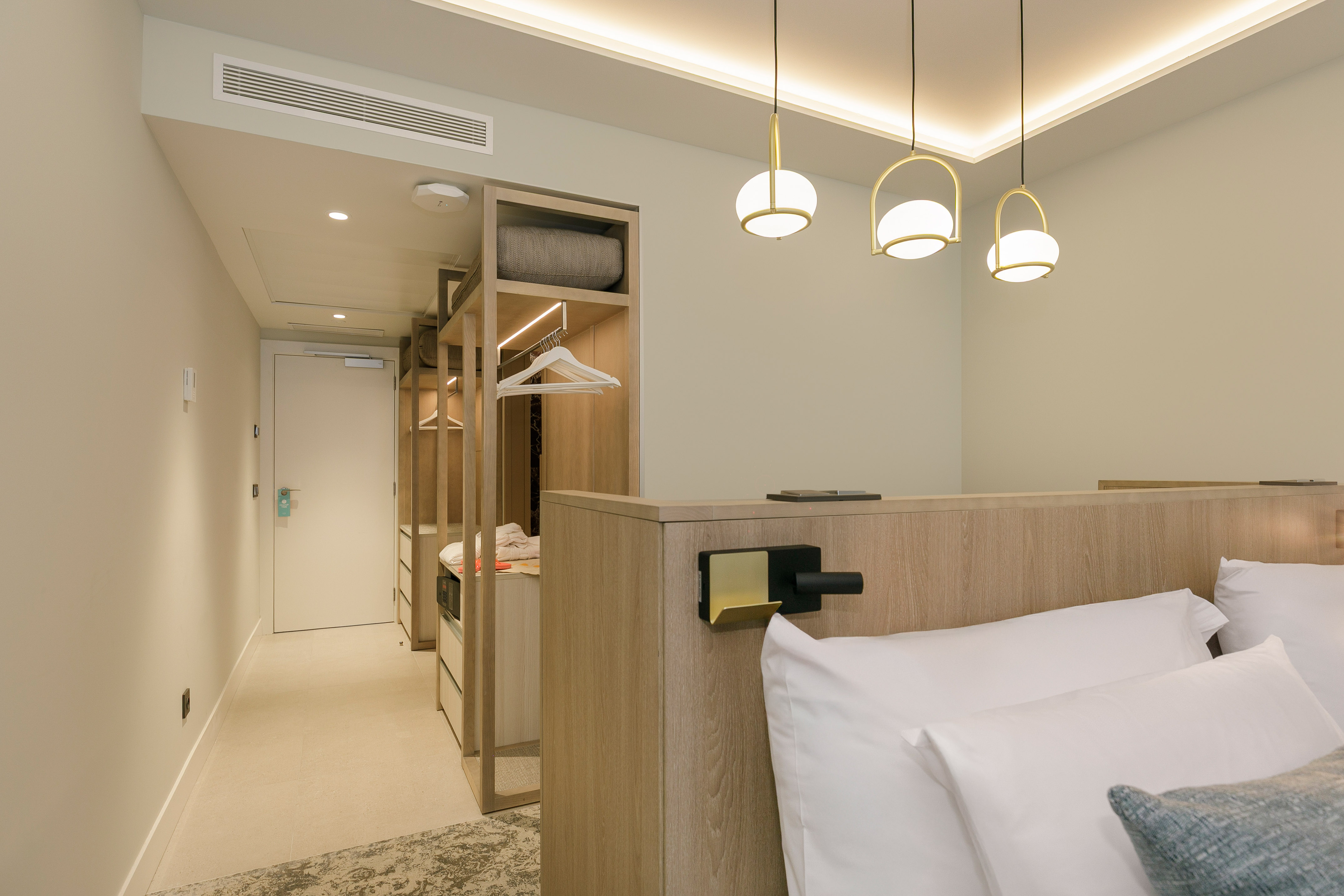 Modern hotel room with bed, wooden headboard, stylish lighting, and open closet.