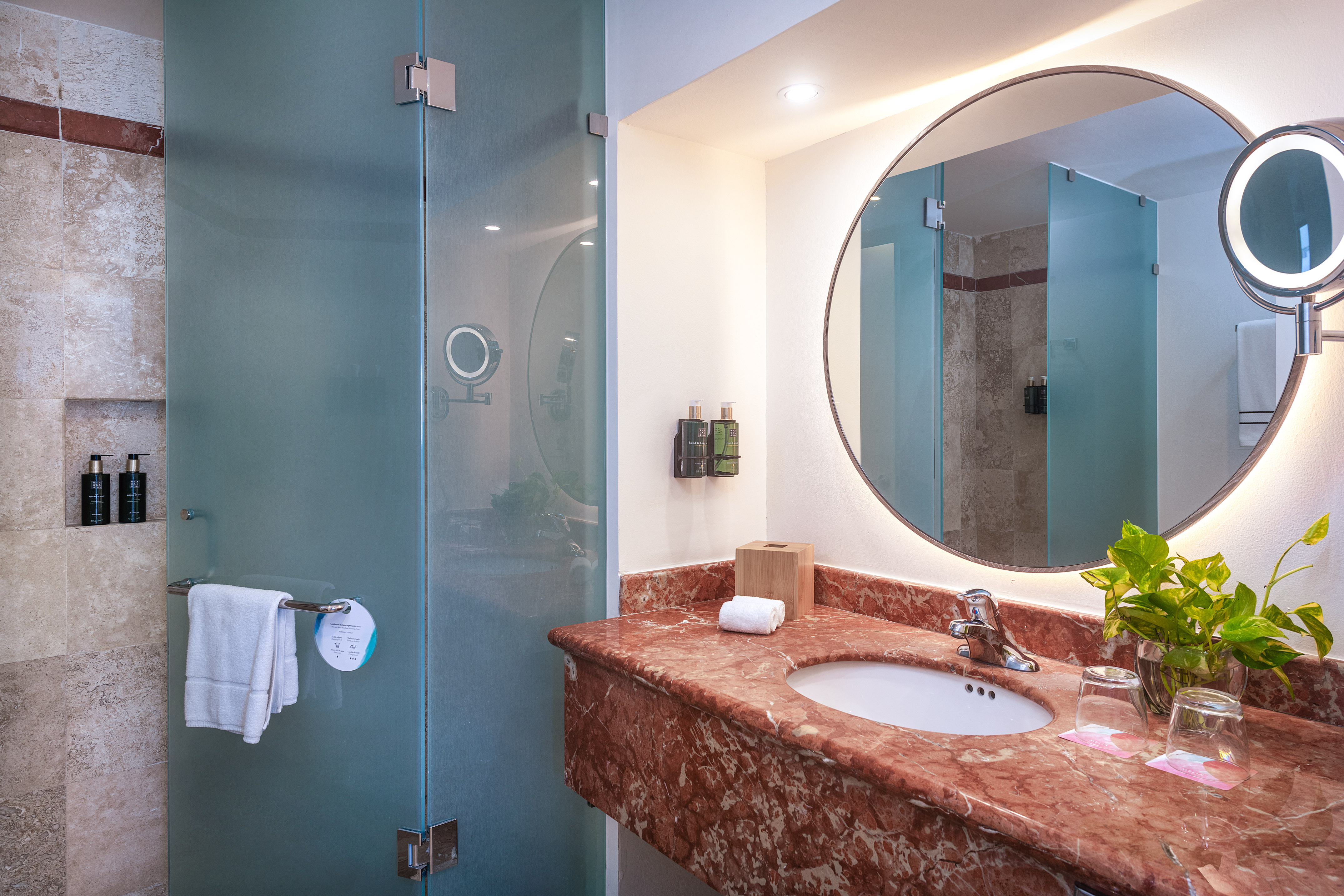 Modern bathroom with red marble vanity, round backlit mirror, and frosted glass shower.
