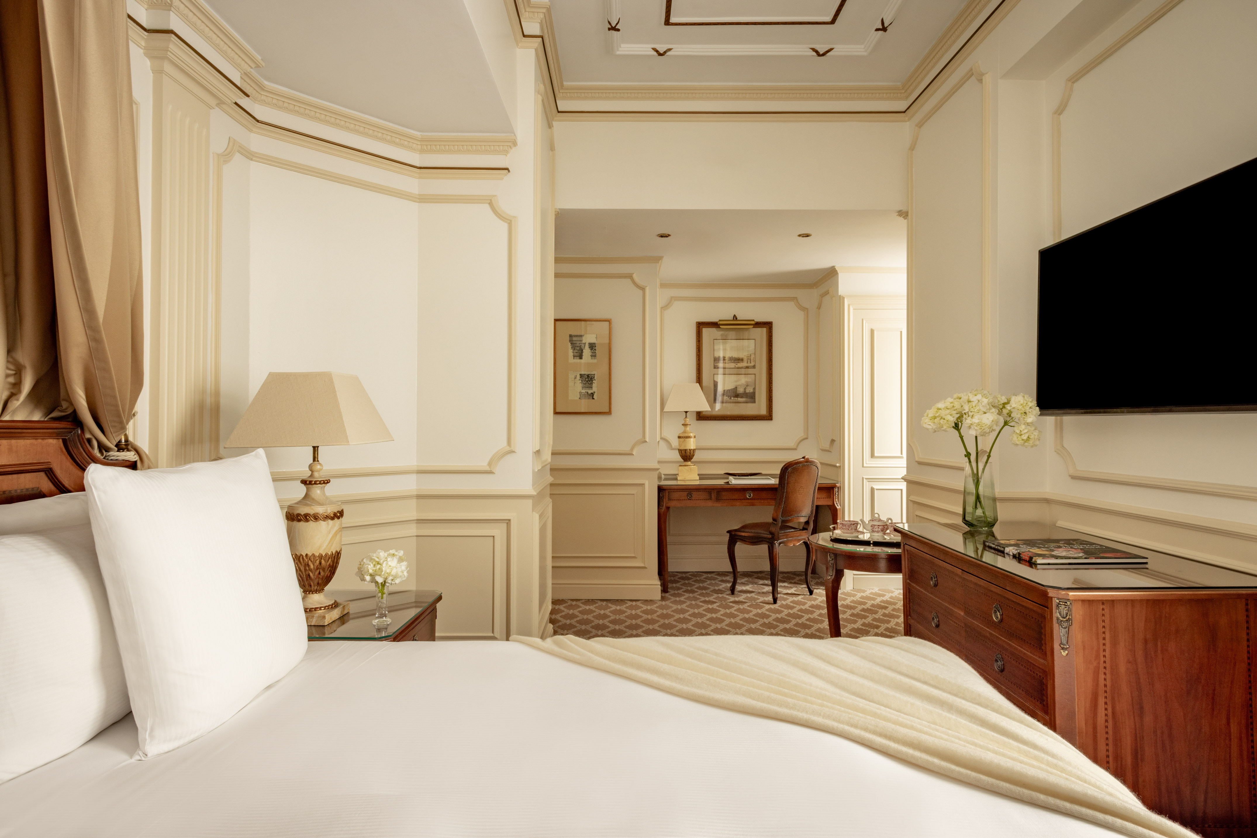 Luxurious hotel suite bedroom with classic decor, large bed, and separate office space.