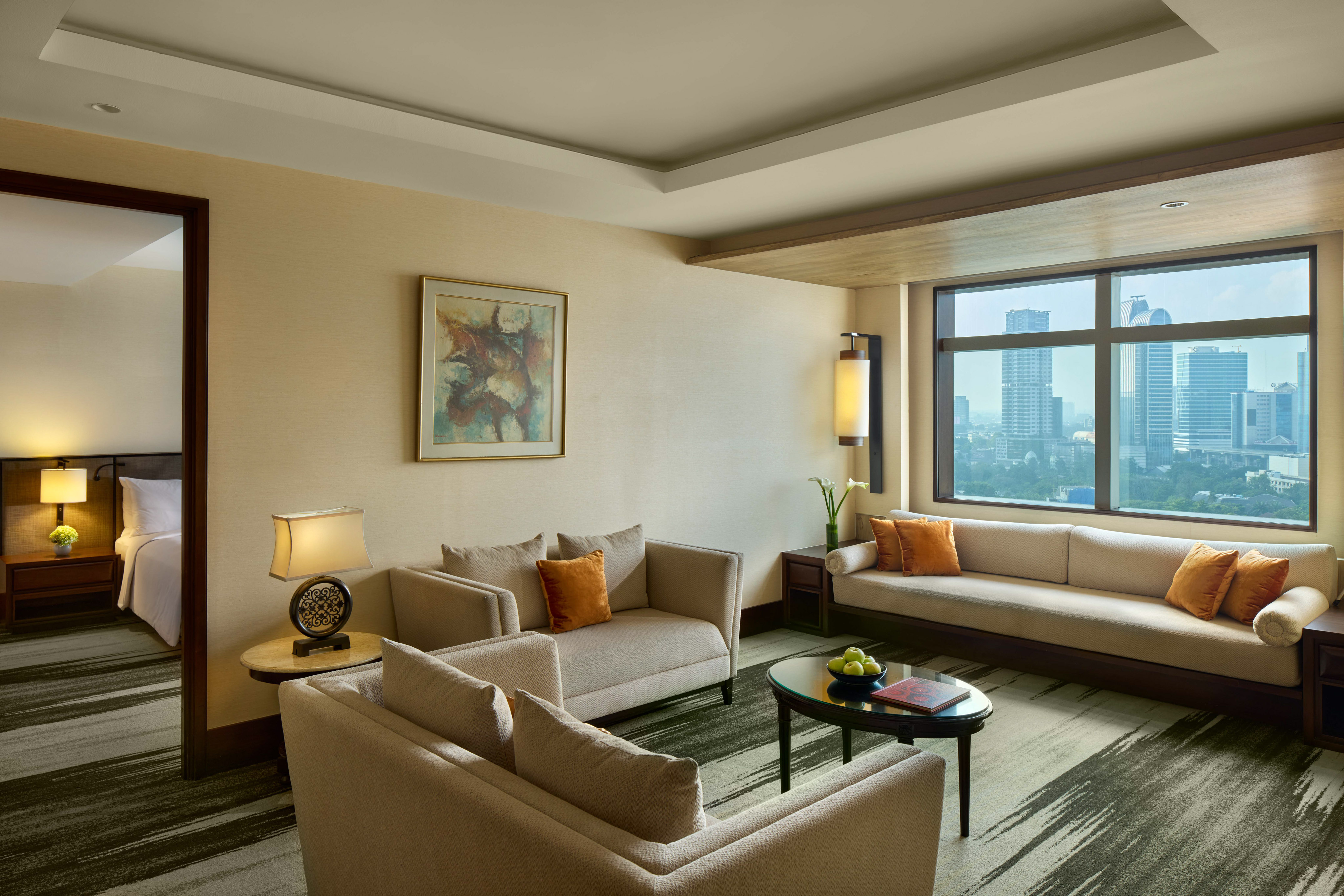 Luxury hotel suite living room with city view, beige sofas, and modern decor.