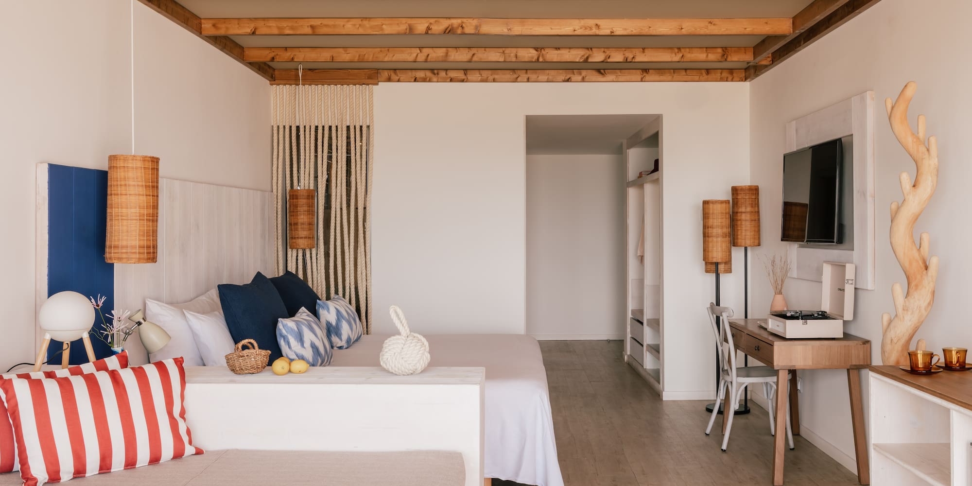 Bohemian bedroom with wooden beams, white bed, wicker lamps, and coastal decor.