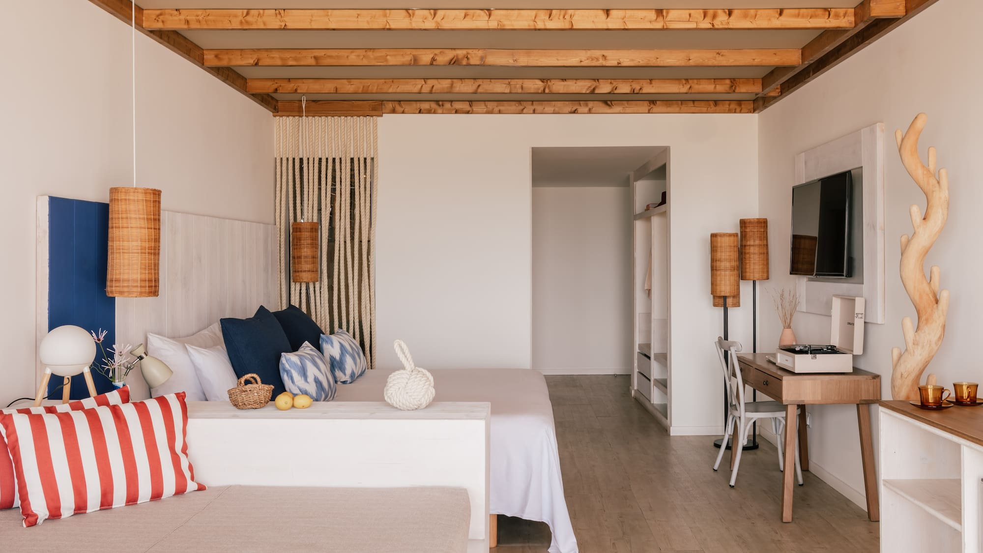 Bohemian bedroom with wooden beams, white bed, wicker lamps, and coastal decor.
