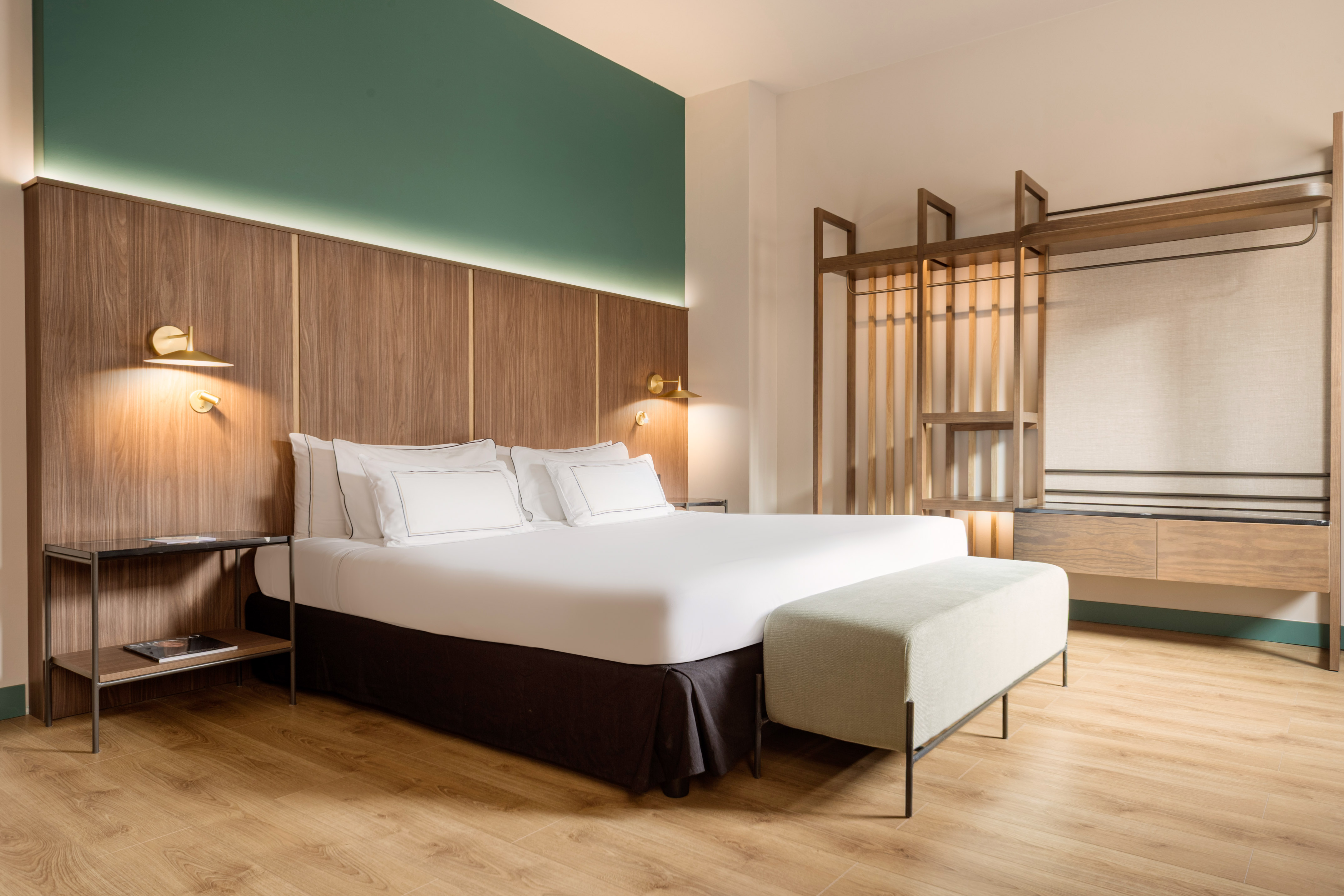 Modern hotel bedroom with king bed, wood headboard, green accent wall, open closet.