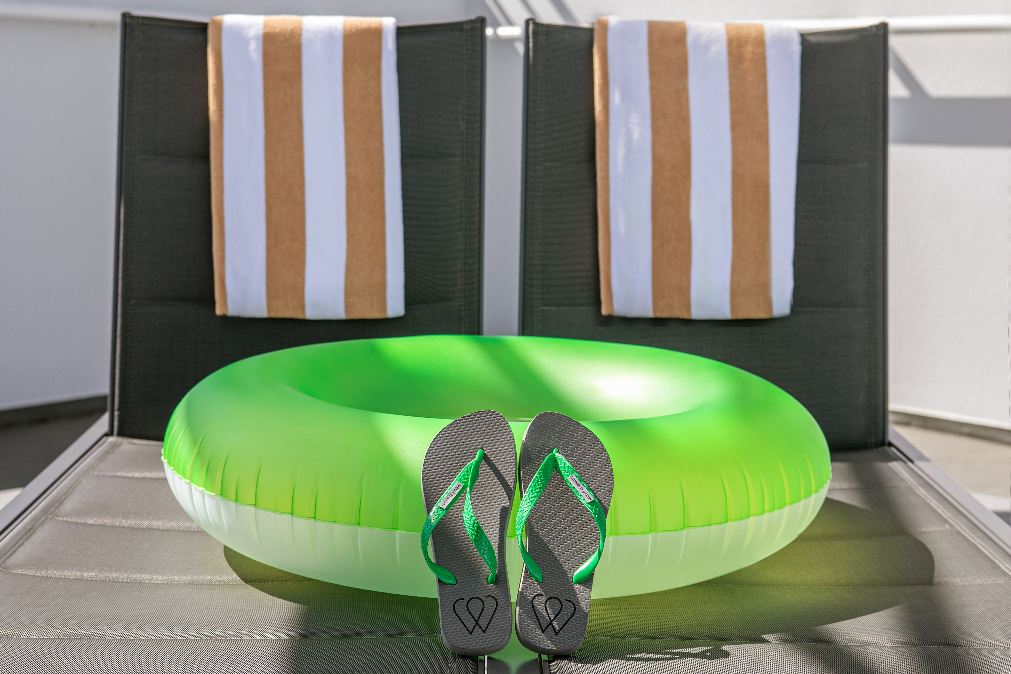 Summer pool scene with green float, flip-flops, and towels on lounge chairs.