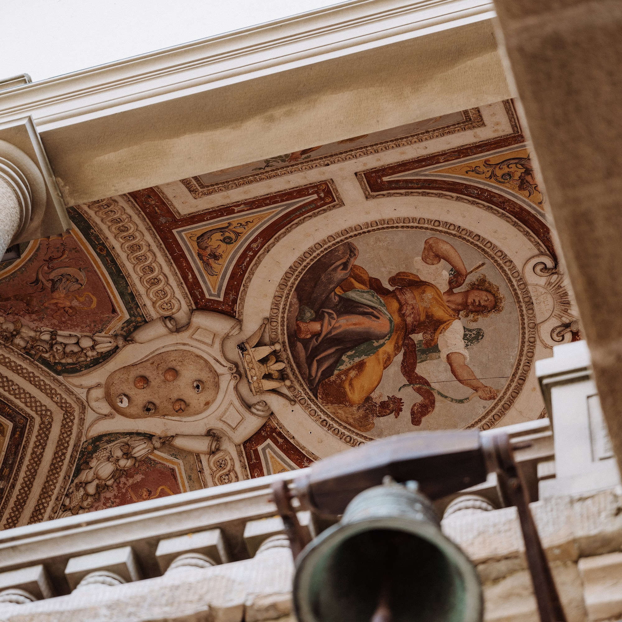 Renaissance ceiling fresco with classical figure and ornate hanging bell.