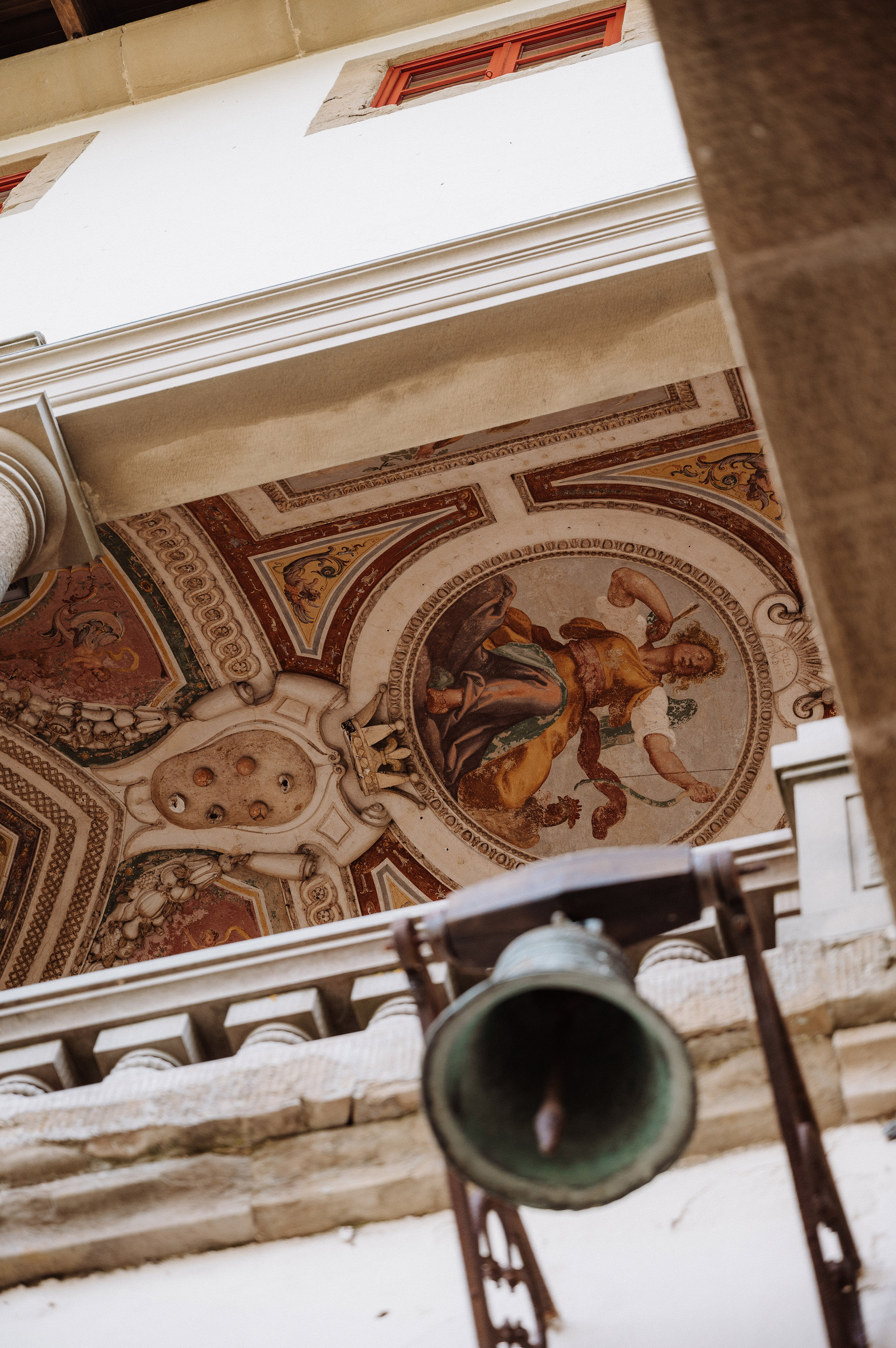 Renaissance ceiling fresco with classical figure and ornate hanging bell.