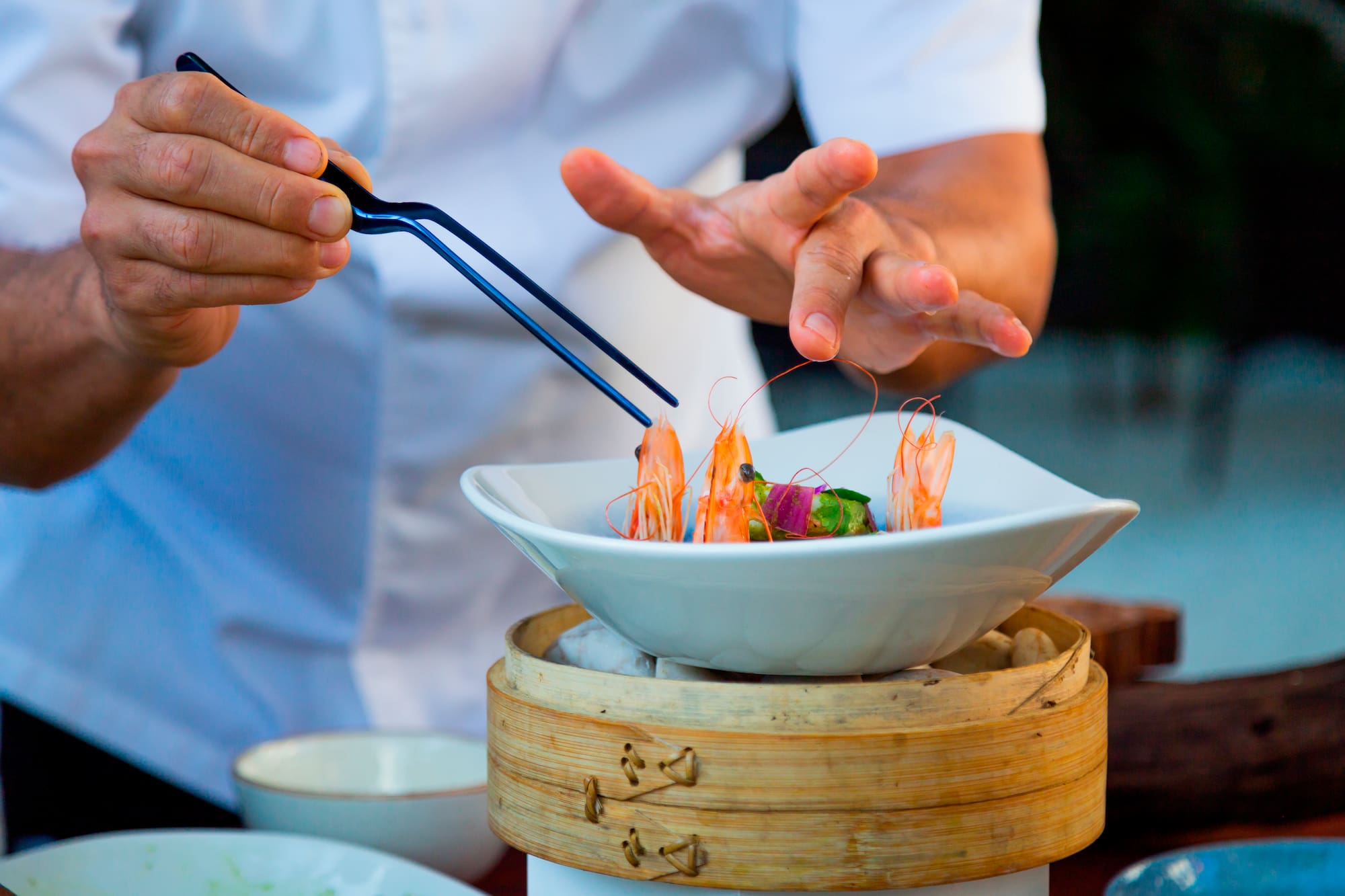 a person holding tongs to a bowl of food