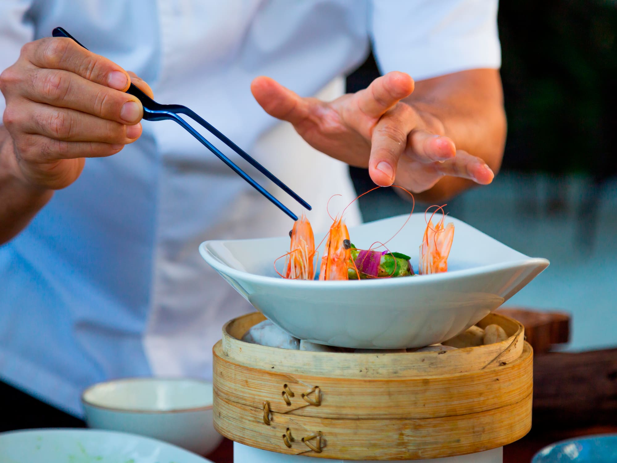 a person holding tongs to a bowl of food