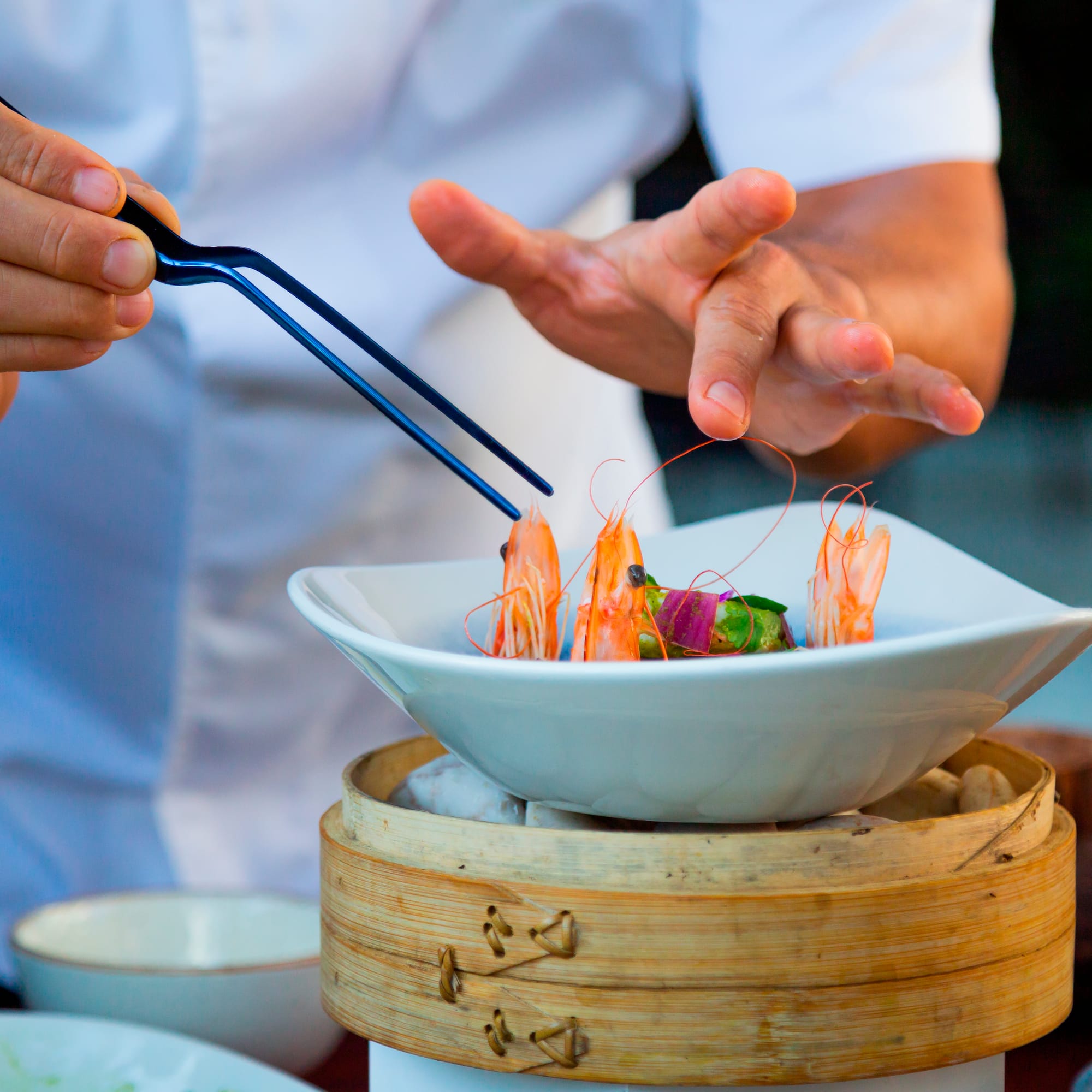 a person holding tongs to a bowl of food