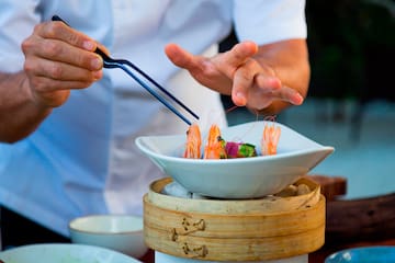 a person holding tongs to a bowl of food