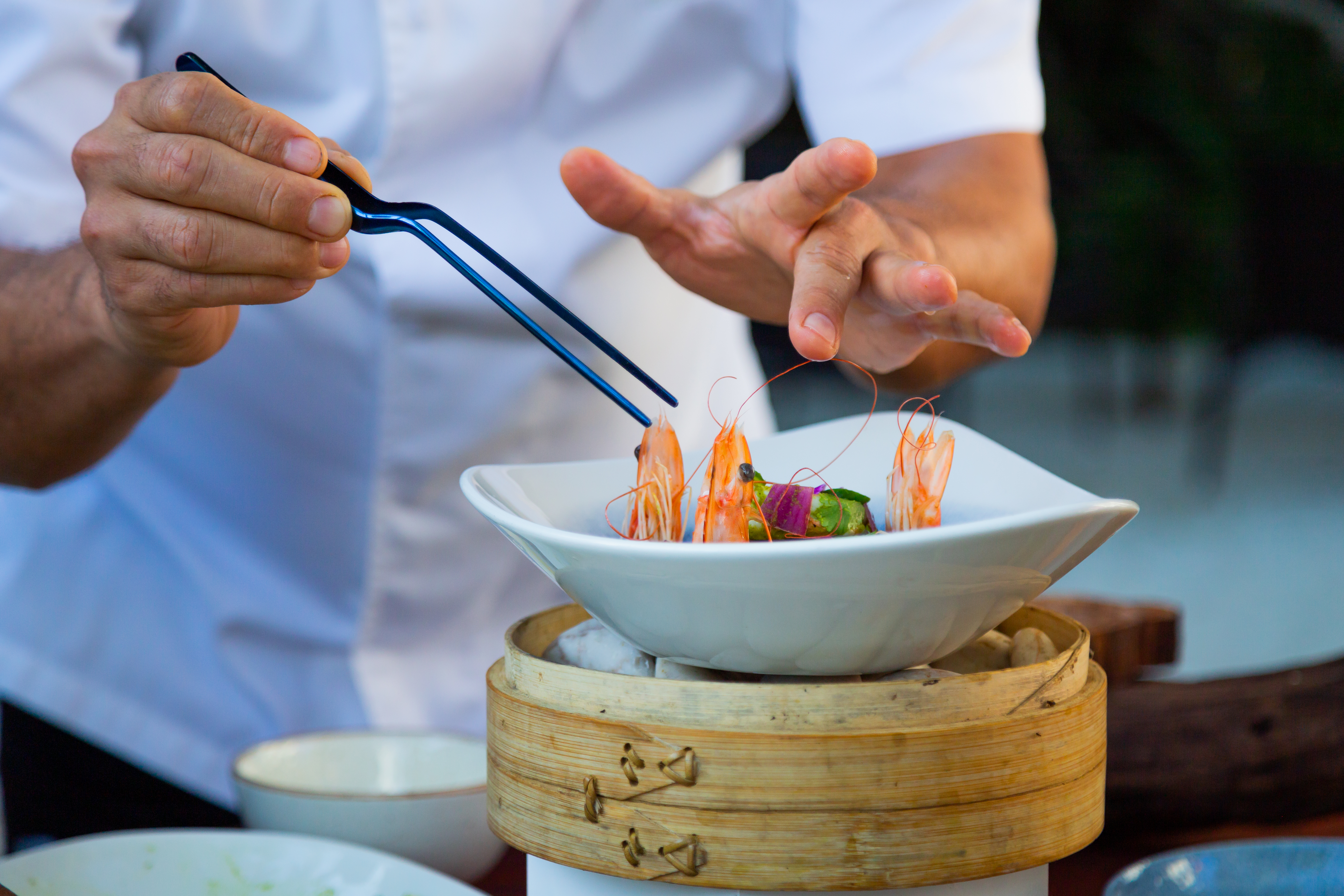 a person holding tongs to a bowl of food