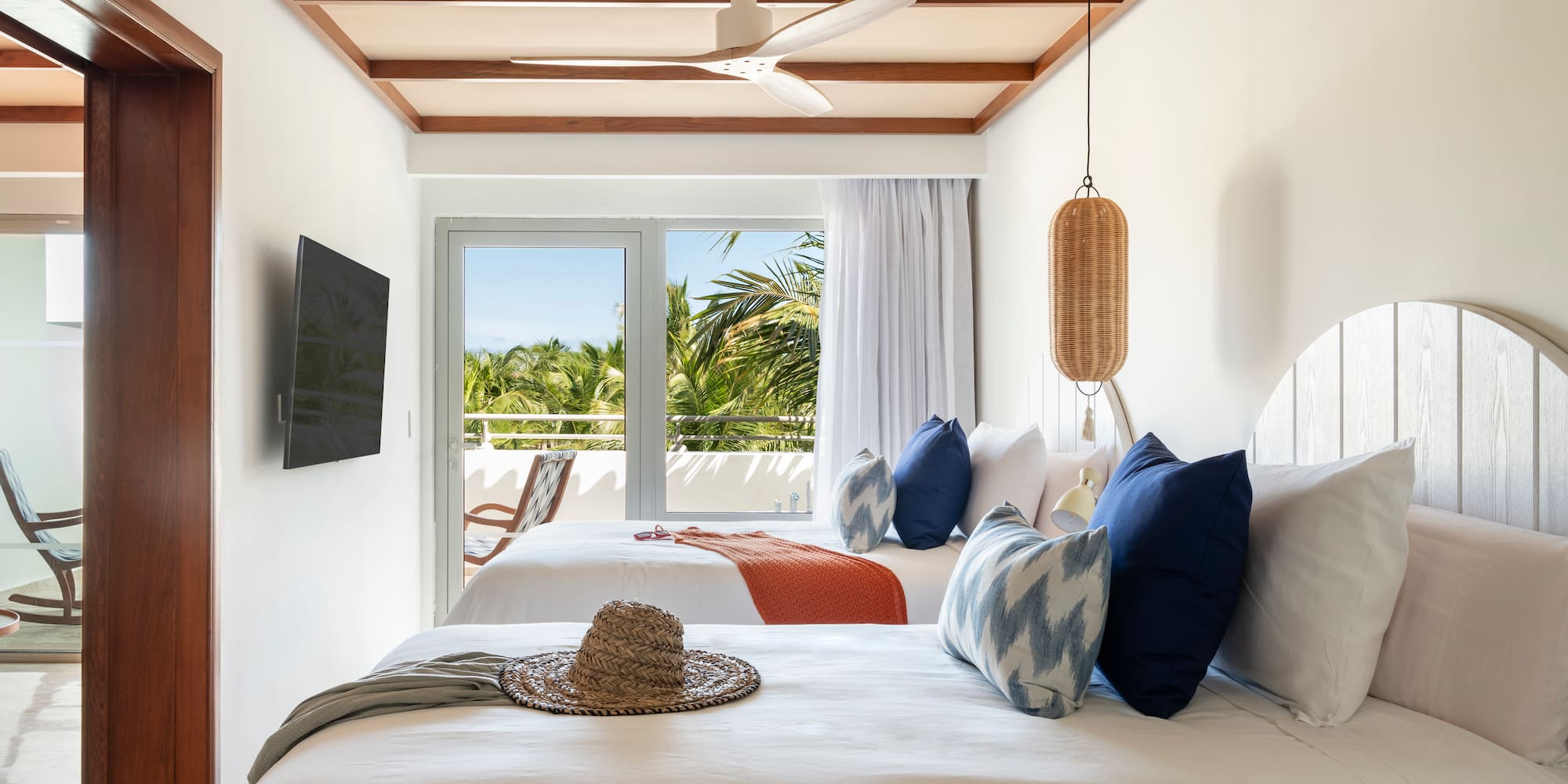 Tropical hotel room with two beds, balcony, palm trees, and ceiling fan.